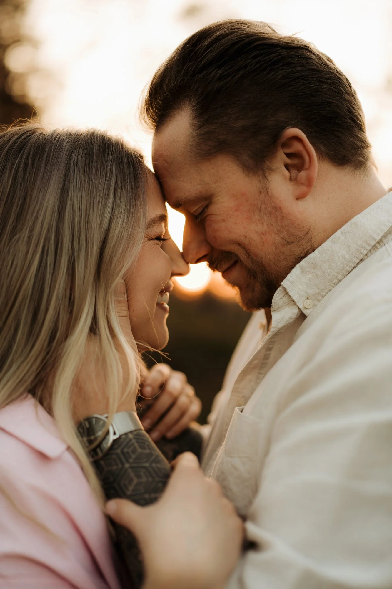 Ein Paar mit gesenktem Kopf, die Stirn an Stirn berühren, in einer romantischen Umarmung bei Sonnenuntergang.