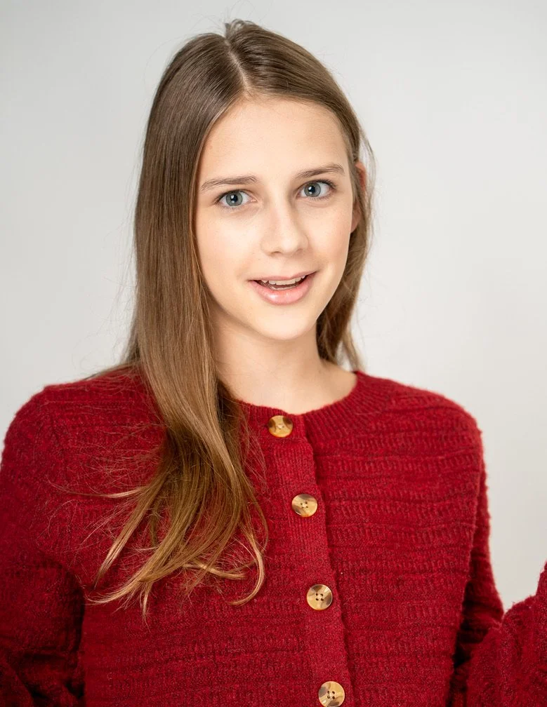 A young woman with long, straight, light brown hair wearing a red sweater with gold buttons, smiling slightly with a neutral background.