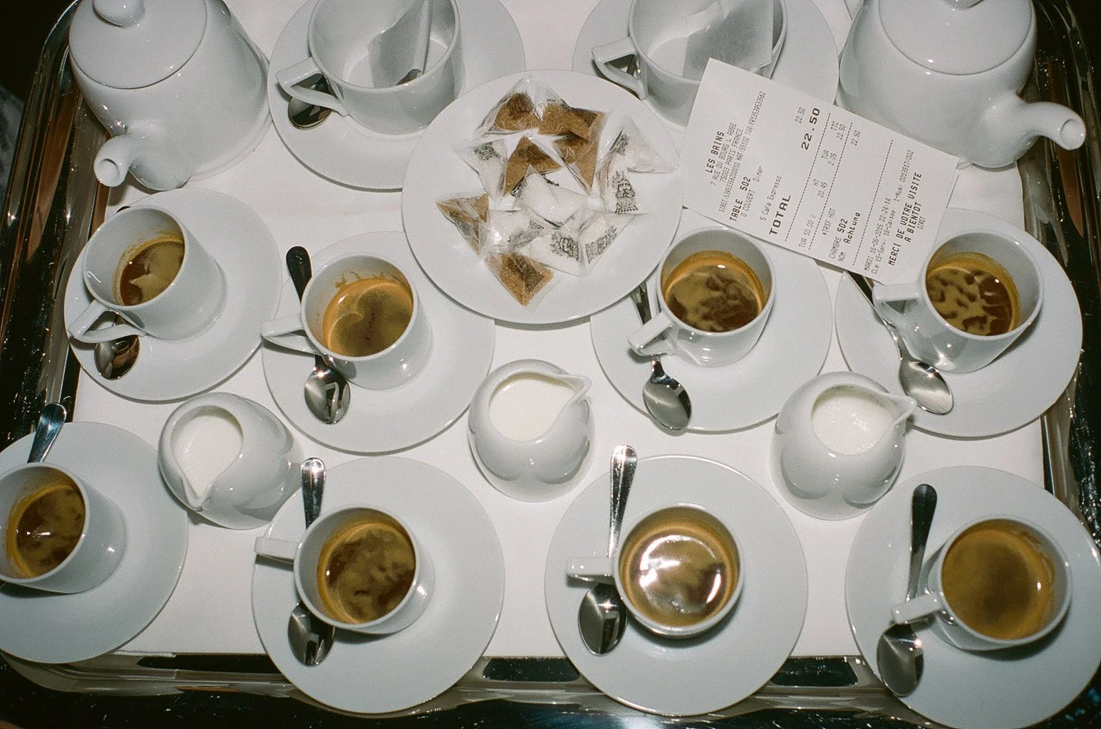 A tray with eight cups of coffee, two teapots, and a platter of sugar packets, with a receipt on top of the tray.