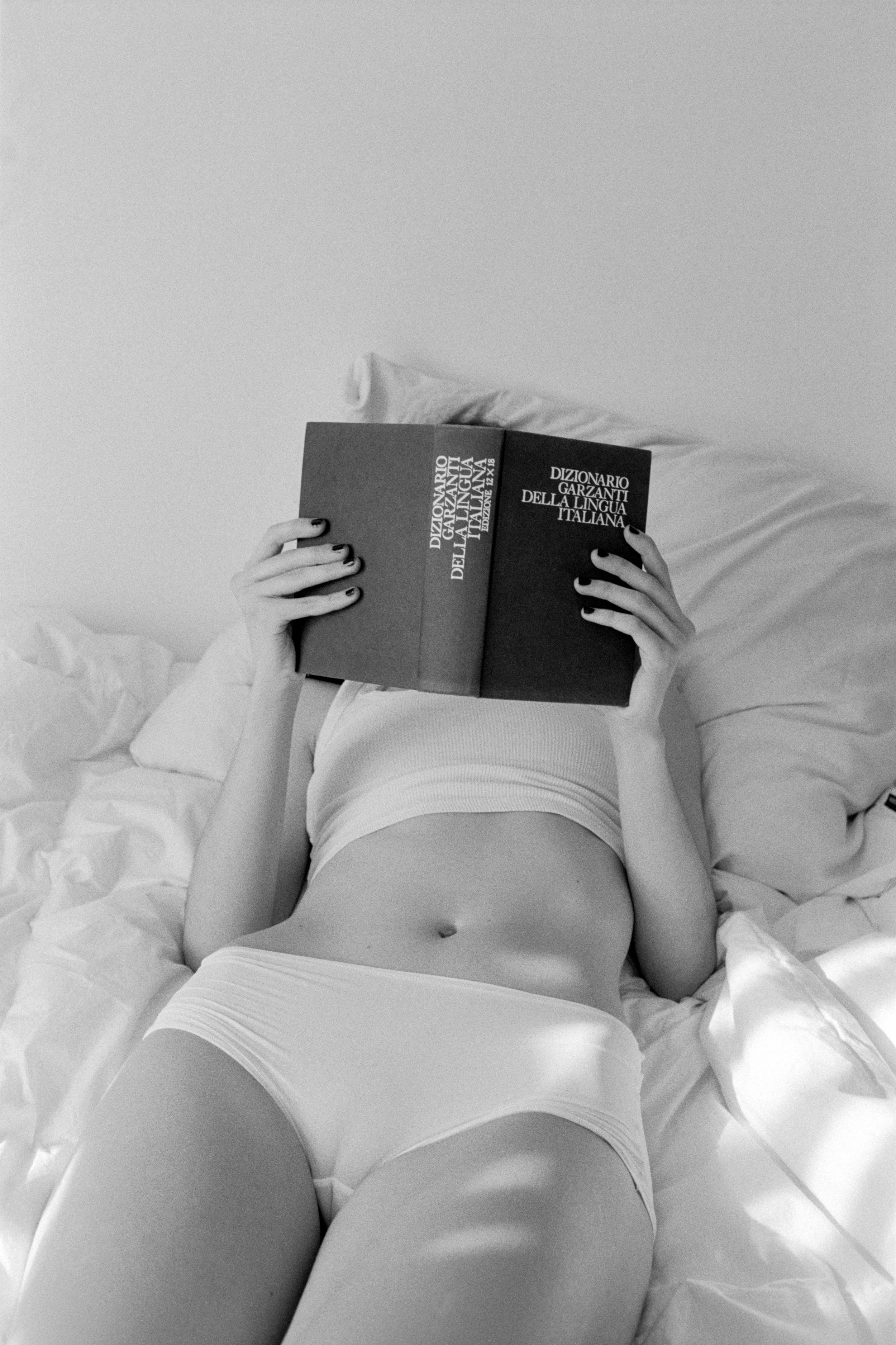 A person lying in bed reading a book, with only their torso and legs visible, in black and white.