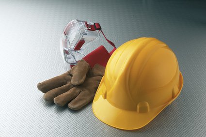 Work safety gear including a yellow hard hat, safety goggles, and work gloves placed on a gray surface.