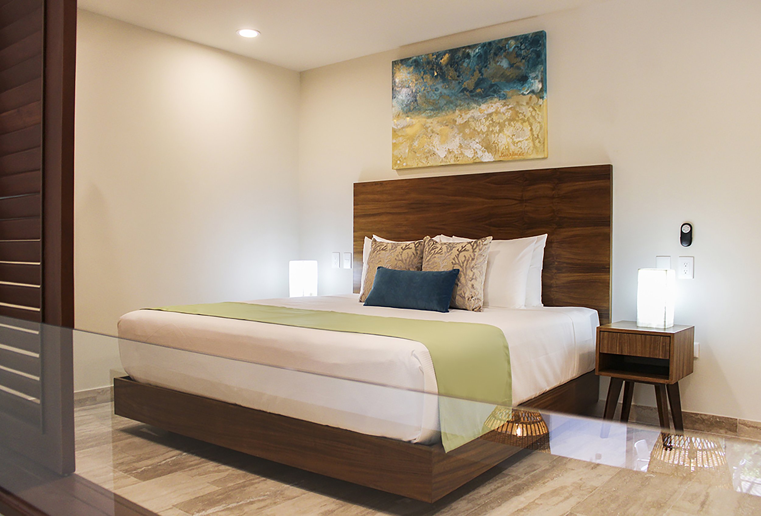Habitación con cama de madera, cojines decorativos, cuadro abstracto en la pared y lámparas