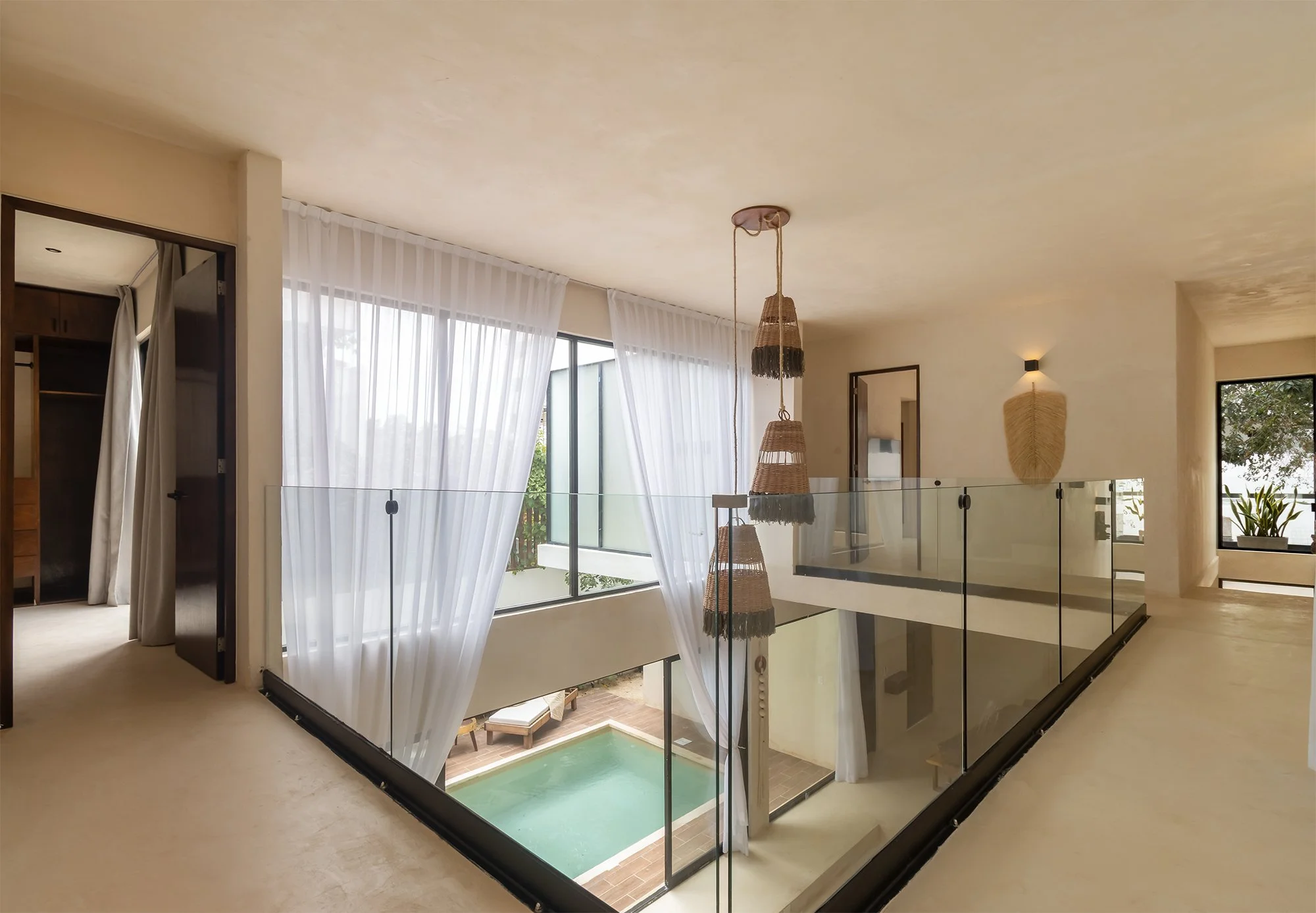 Interiores de una casa moderna con piscina cubierta, ventanas grandes con cortinas blancas y decoración simple en tonos neutros.