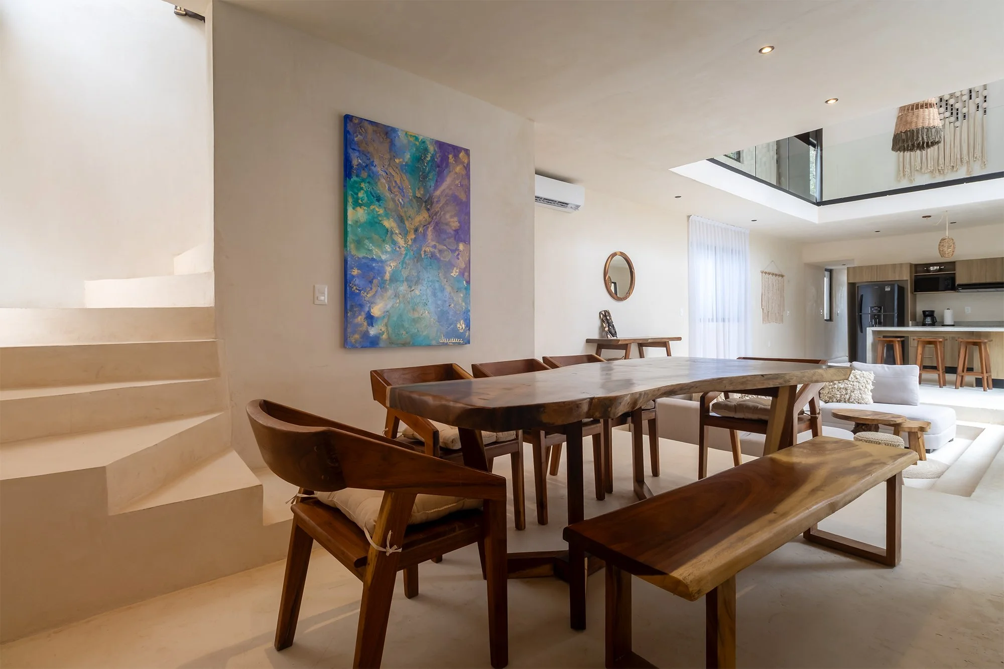 Interior de sala con mesa de madera y sillas, decorada con obras de arte y muebles de estilo moderno y rústico.
