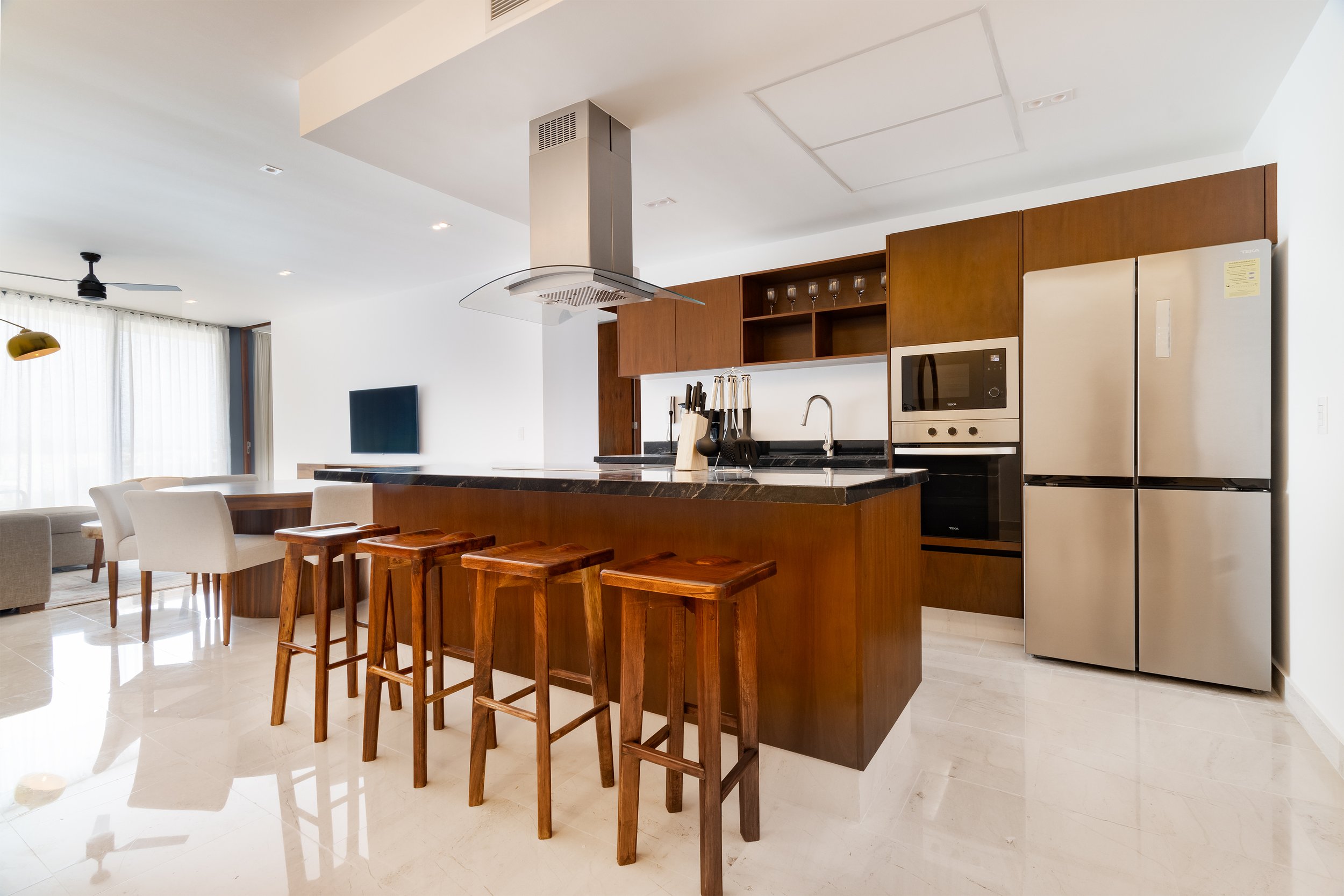 Cocina moderna con isla de madera, barra de granito y puertas de madera, con electrodomésticos de acero inoxidable y utensilios de cocina.