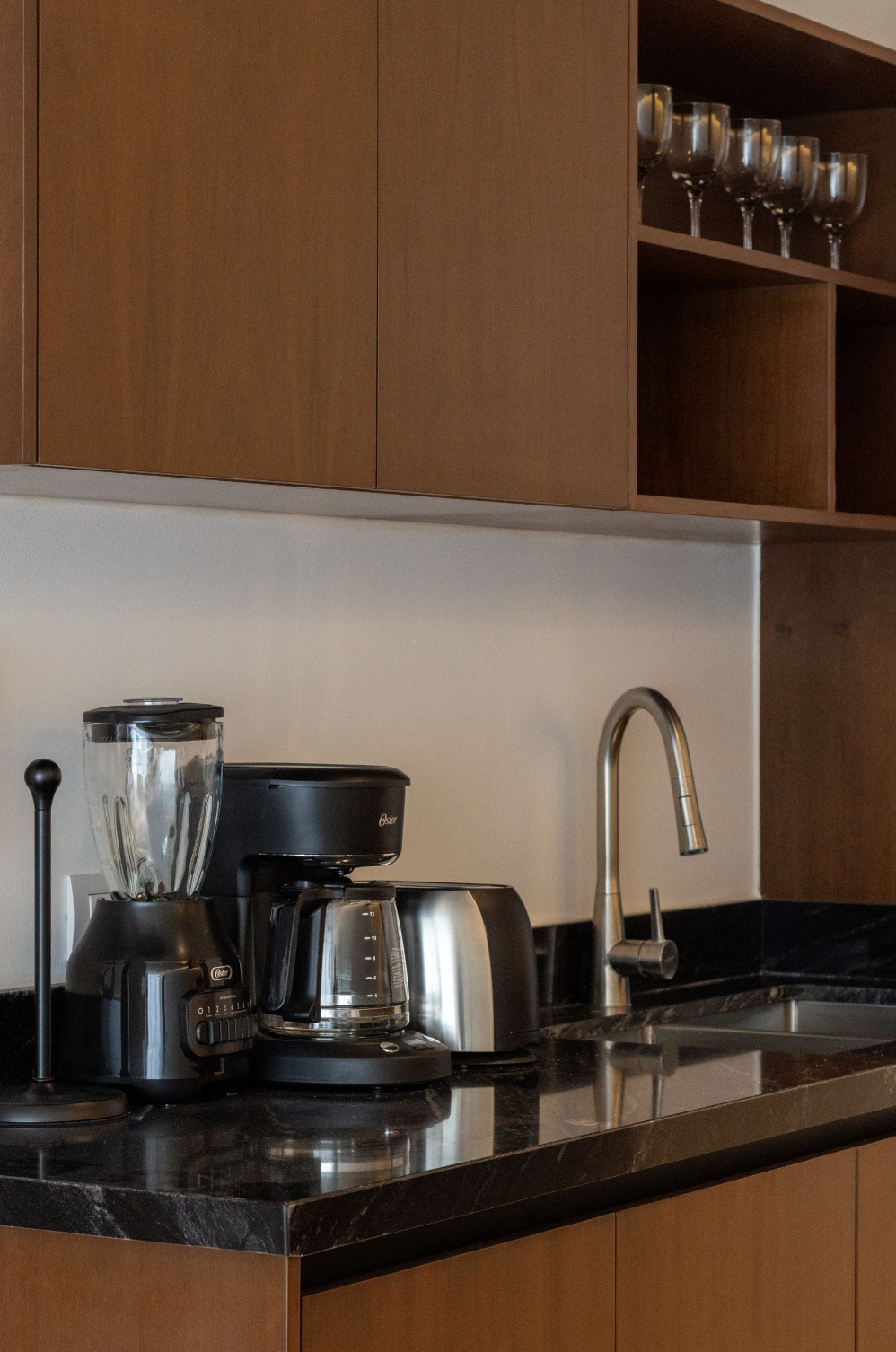 Cafetera, licuadora y tostadora en una encimera de cocina con gabinetes de madera y copas en un estante