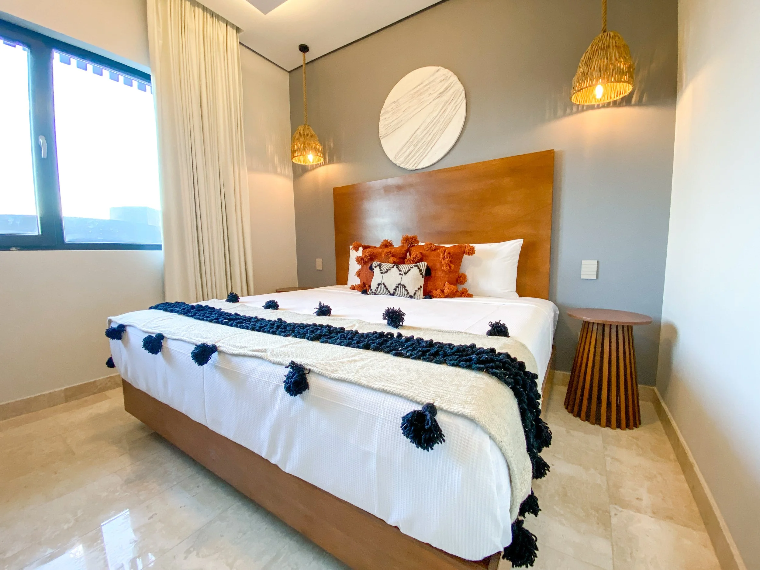 Habitación moderna con cama grande, cabecera de madera, decoraciones en tonos rojos y negros, y luz cálida