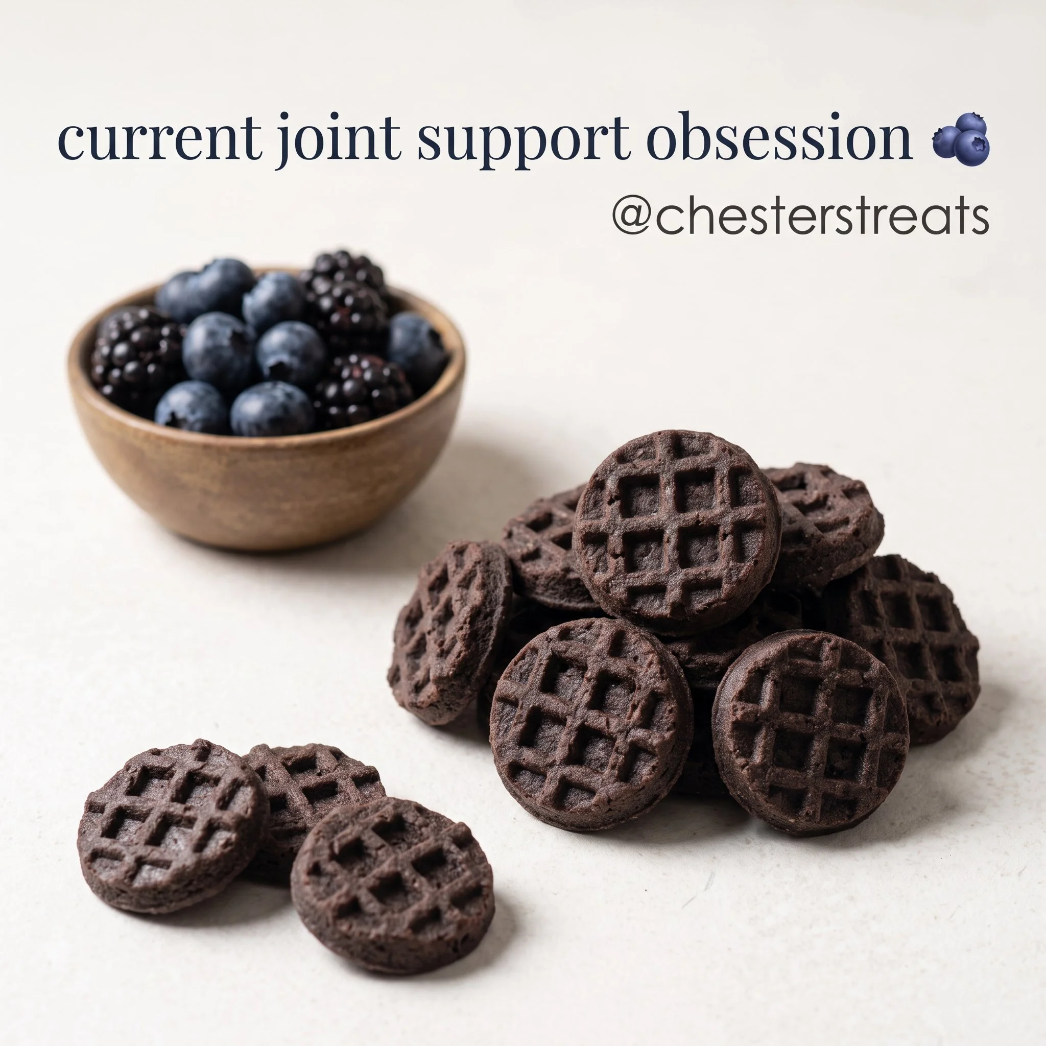 A small wooden bowl filled with fresh blueberries and blackberries on a white surface, with a few chocolate chip cookies arranged nearby.