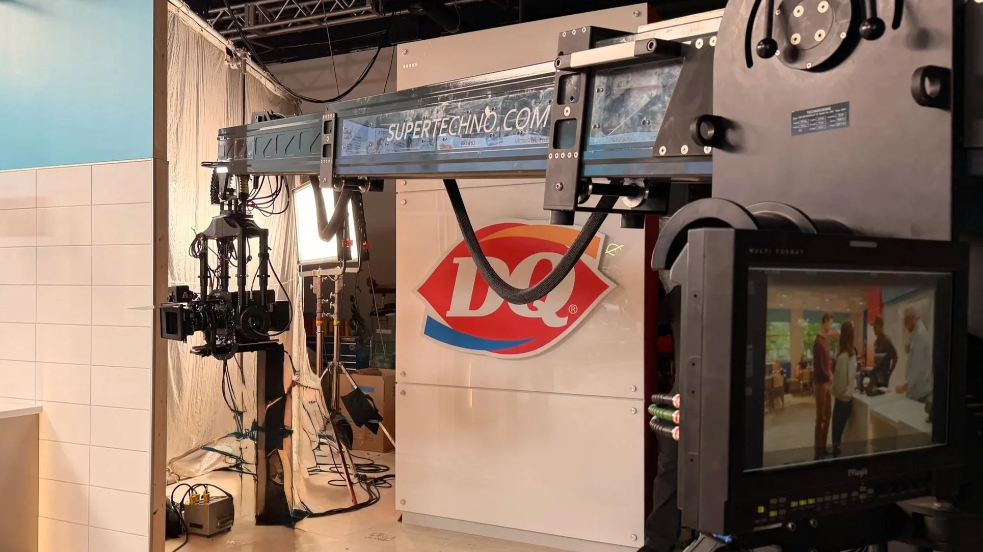 A commercial set with professional equipment, including cameras, lighting, and a monitor. The backdrop features a DQ logo, indicating a Dairy Queen branding or promotional shoot.