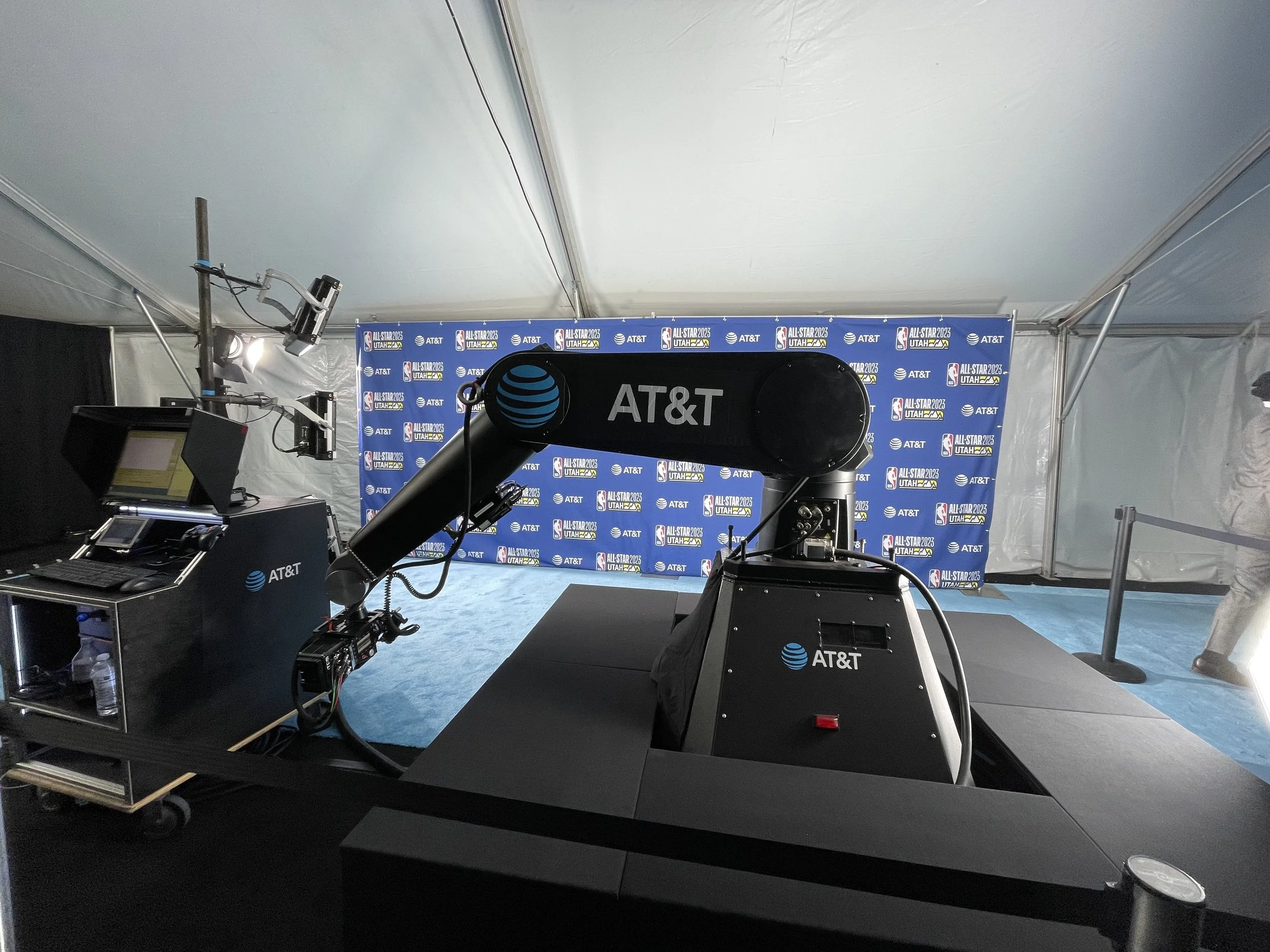 Photo of media equipment setup at an event, with AT&T branding and a backdrop with event logos for All-Star 2023 Utah, inside a tent.