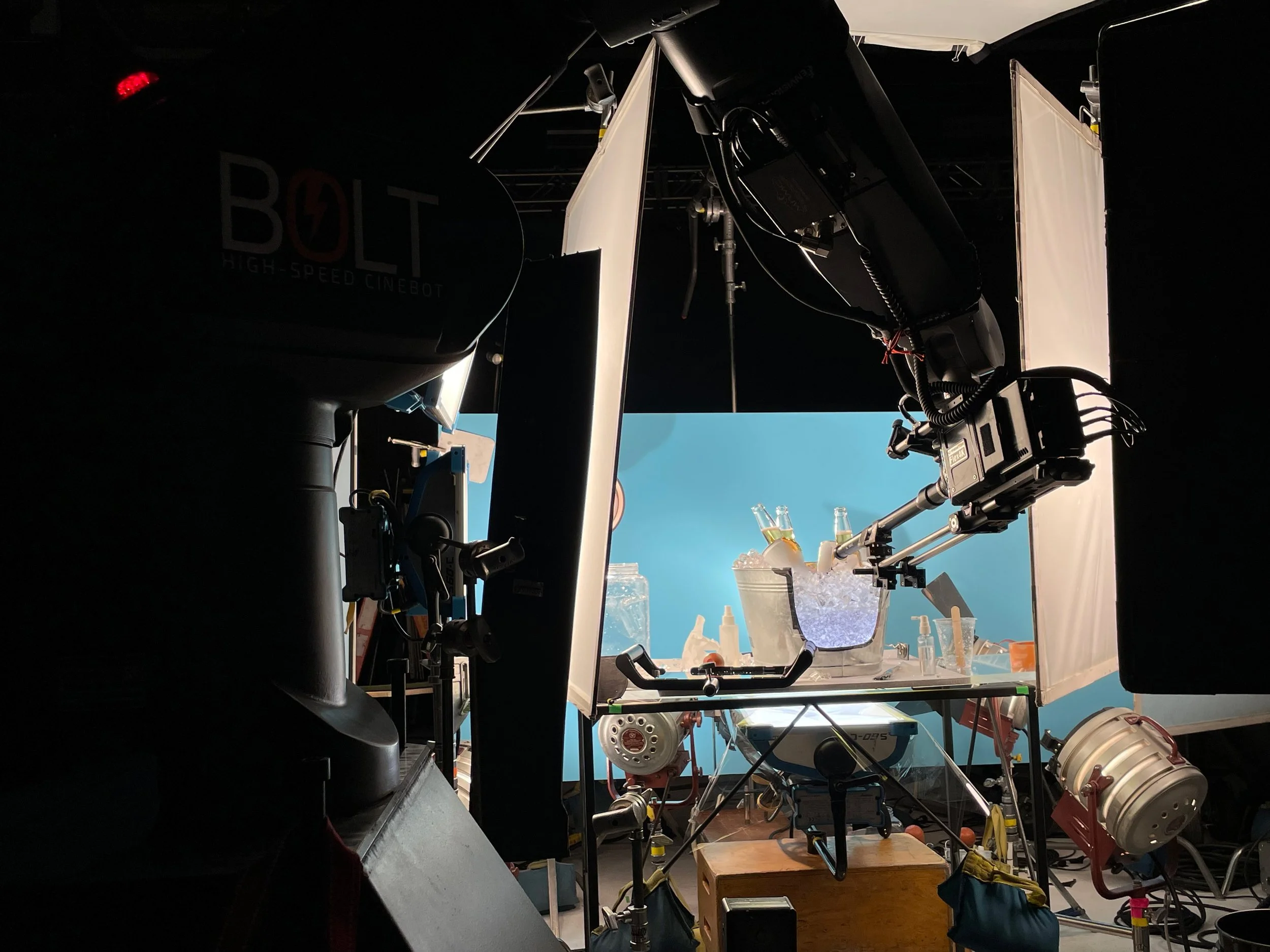 Photography studio setup with professional equipment, including cameras and lighting, with a blue backdrop, various props, and supplies on tables and shelves.