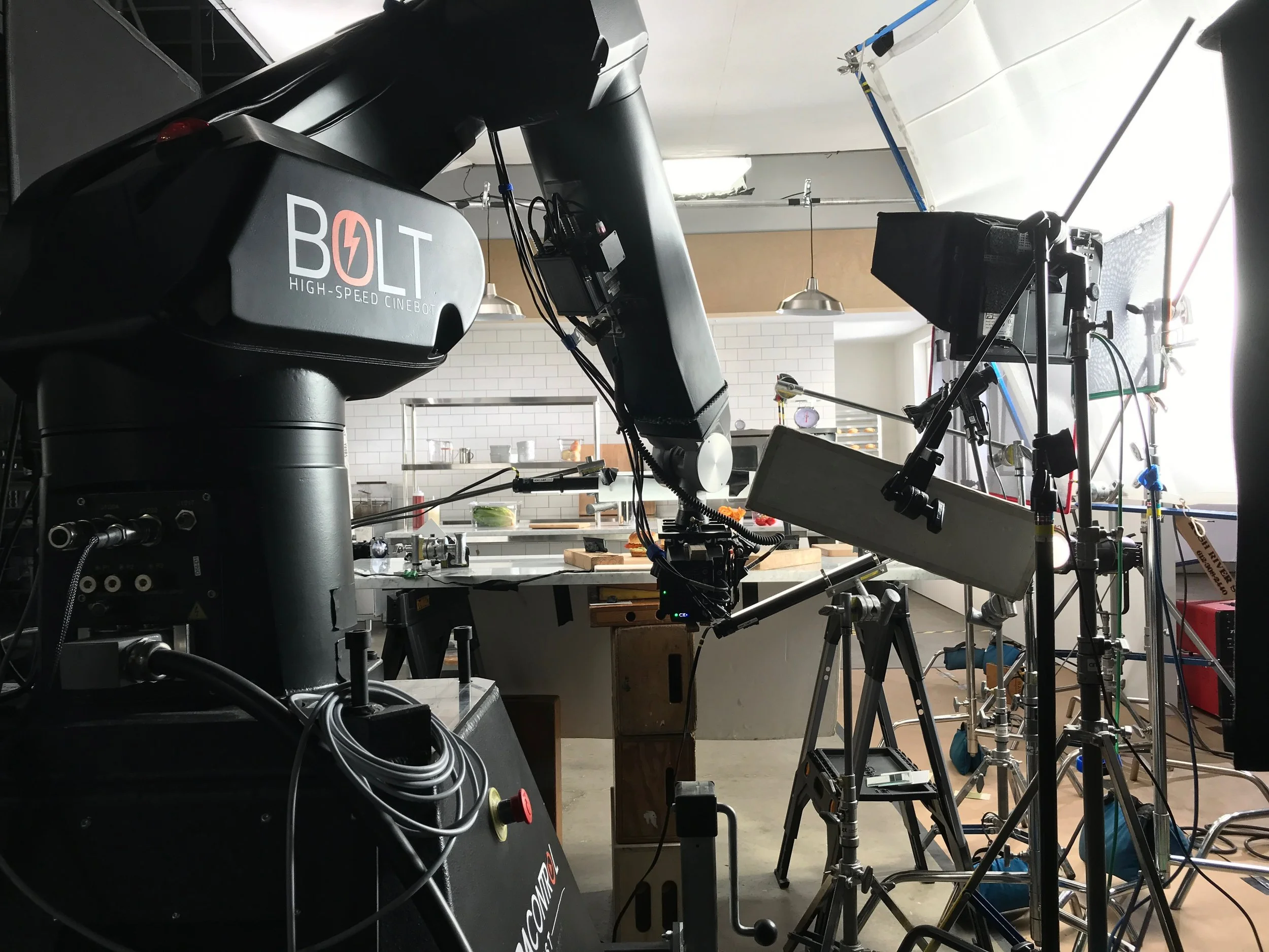 Photograph of a production studio set with professional film equipment including a Bol high-speed Cinebot robot arm, cameras, lighting, and scaffolding in a well-lit industrial space.