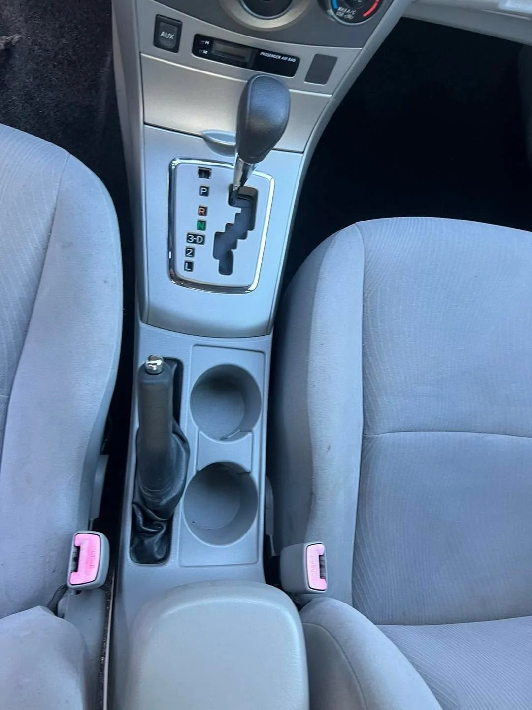Interior view of a car's center console showing an automatic gear shift, a handbrake, cup holders, and portions of the front seats and dashboard.