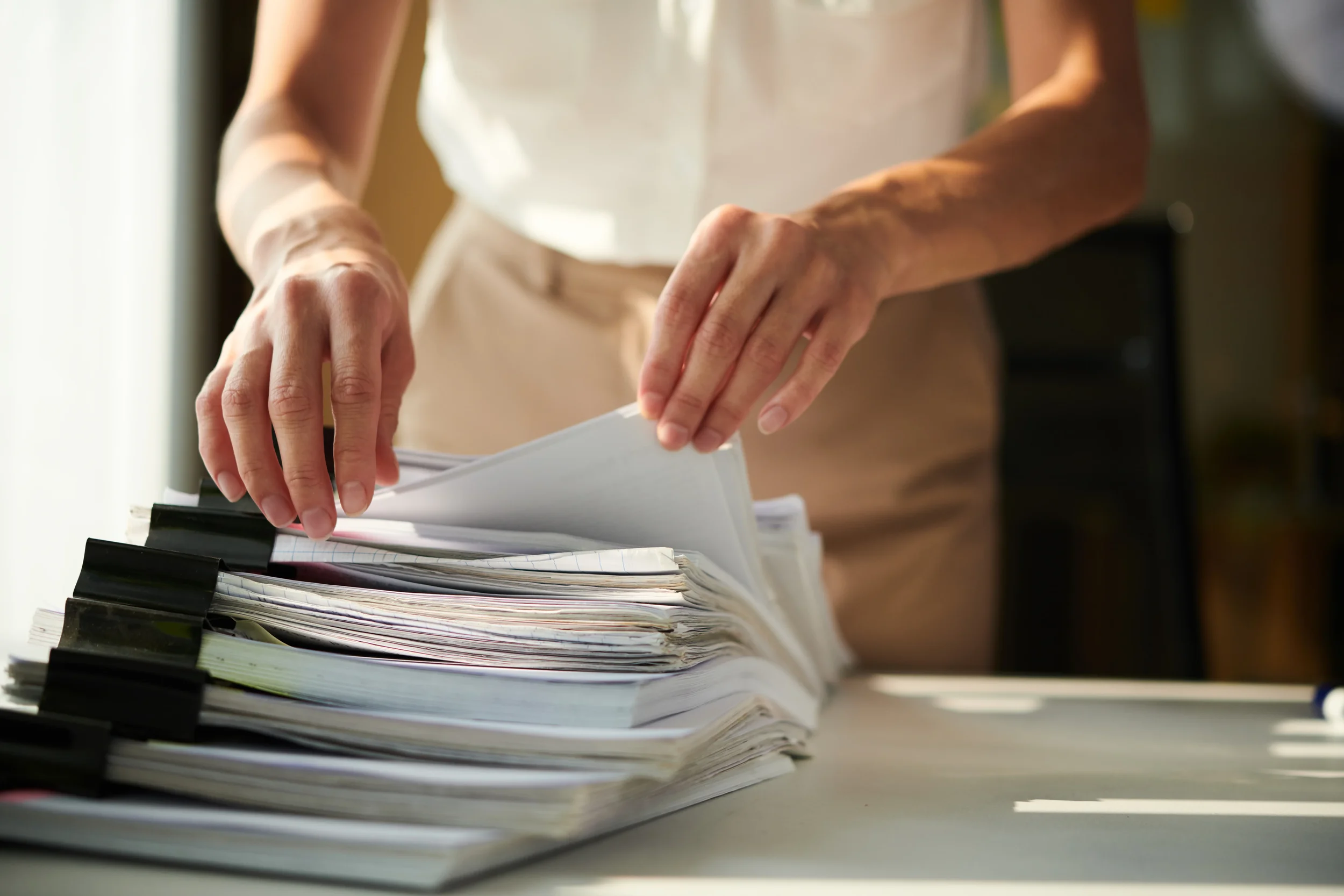 Close-up of a person organizing papers and folders on a desk.