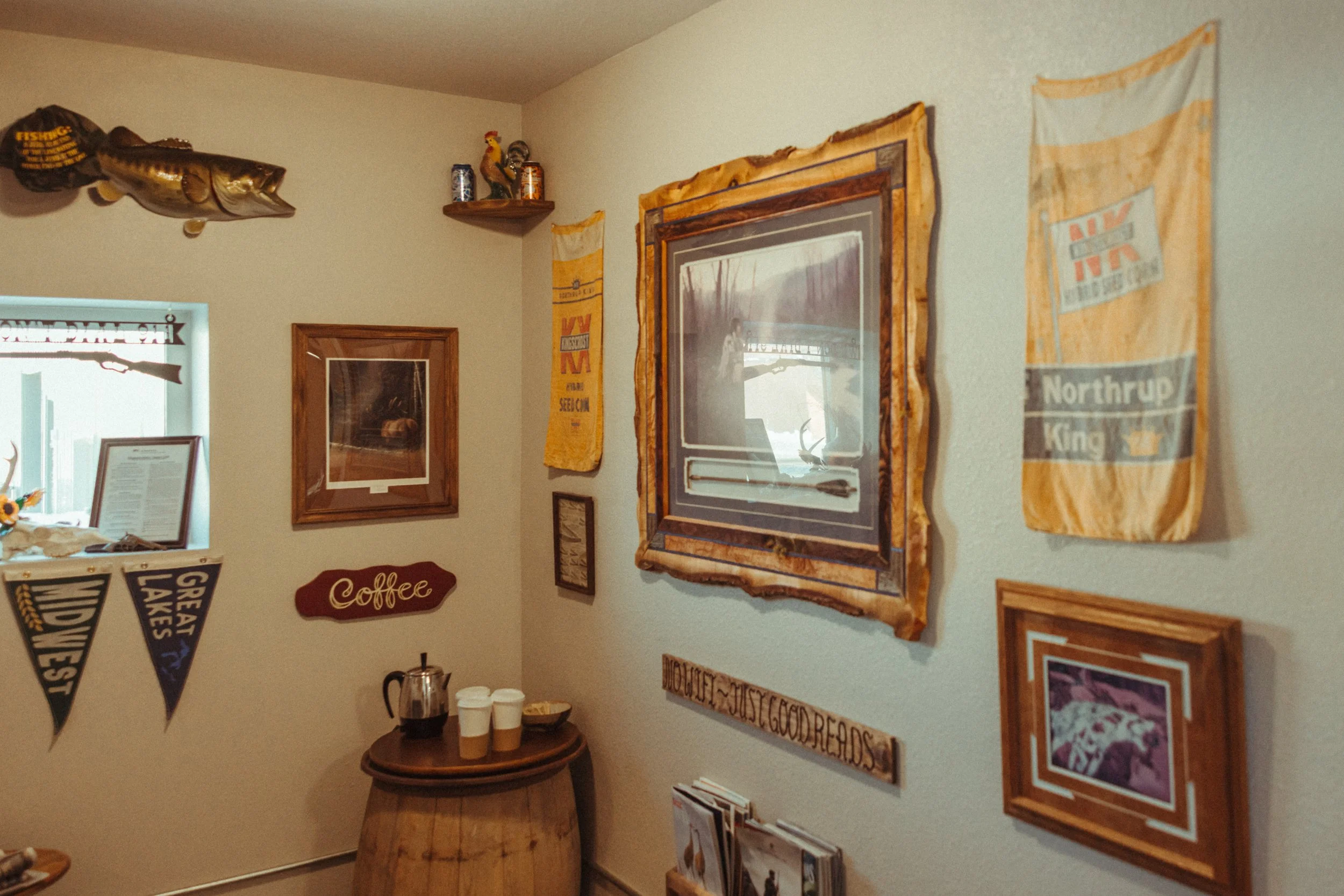 A cozy indoor space decorated with framed artwork, a mounted fish, banners, and a small table with coffee cups and a French press.
