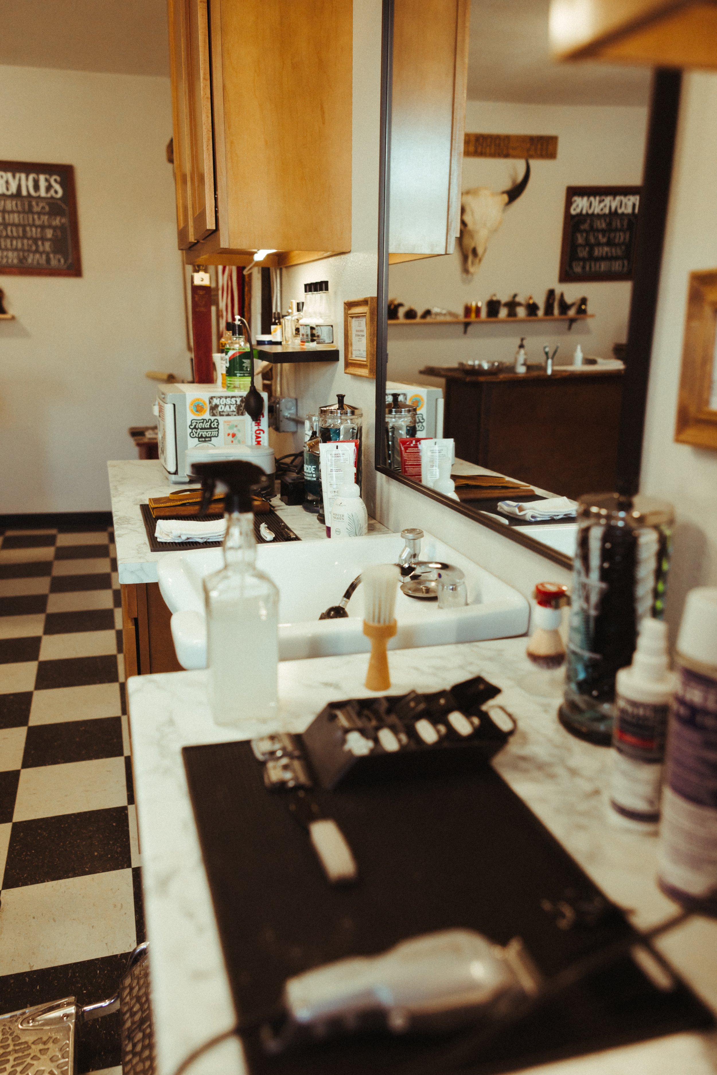 Counter with cleaning supplies, a salt and pepper shaker, and a black mat with a tattoo machine on top, in a kitchen or cafe setting with cabinets and a mirror with a reflection of a room in the background.