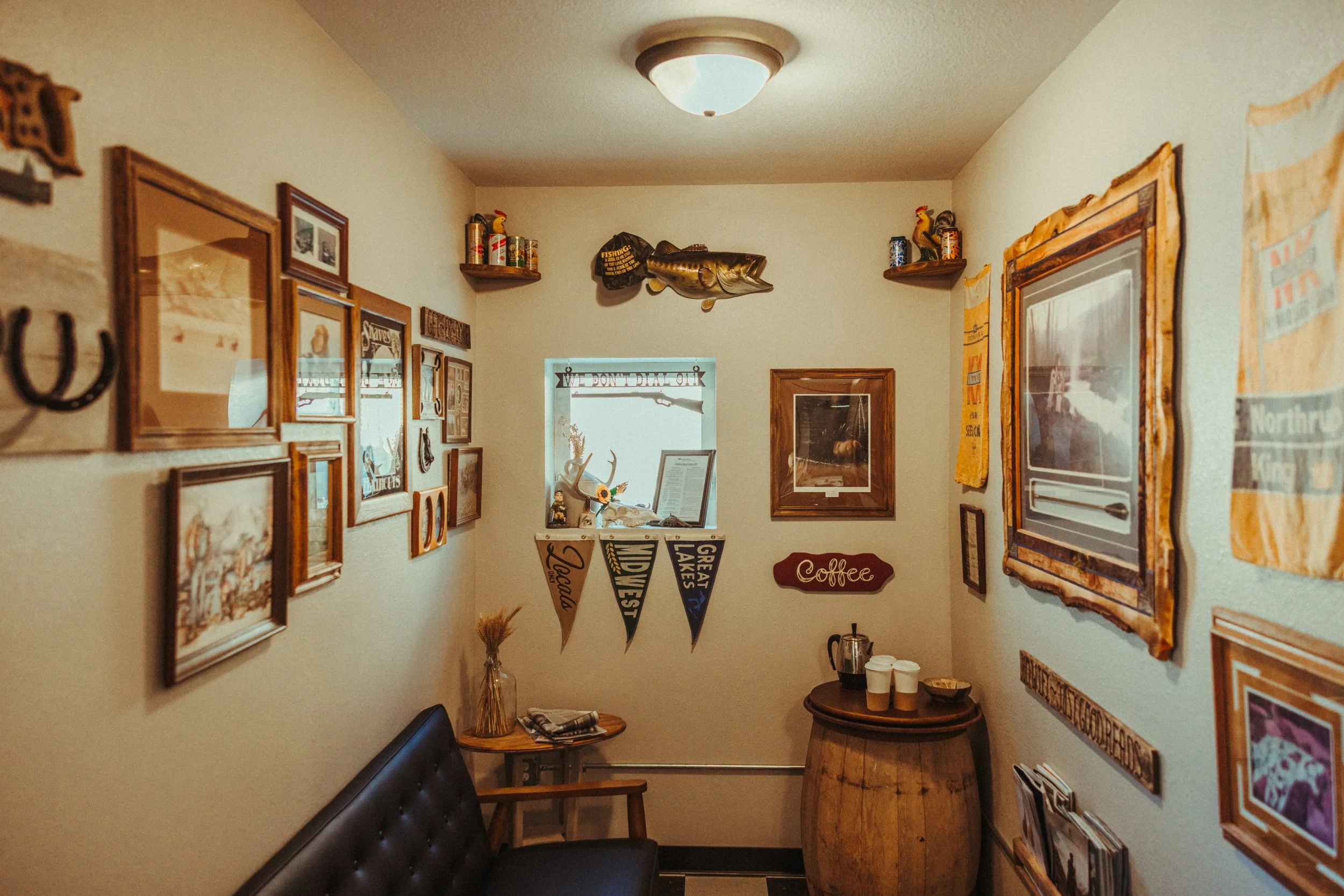 A cozy interior with framed pictures, a fish wall decoration, a shelf with cans and decorative items, a 'Coffee' sign, flags, and small tables with cups and snacks.