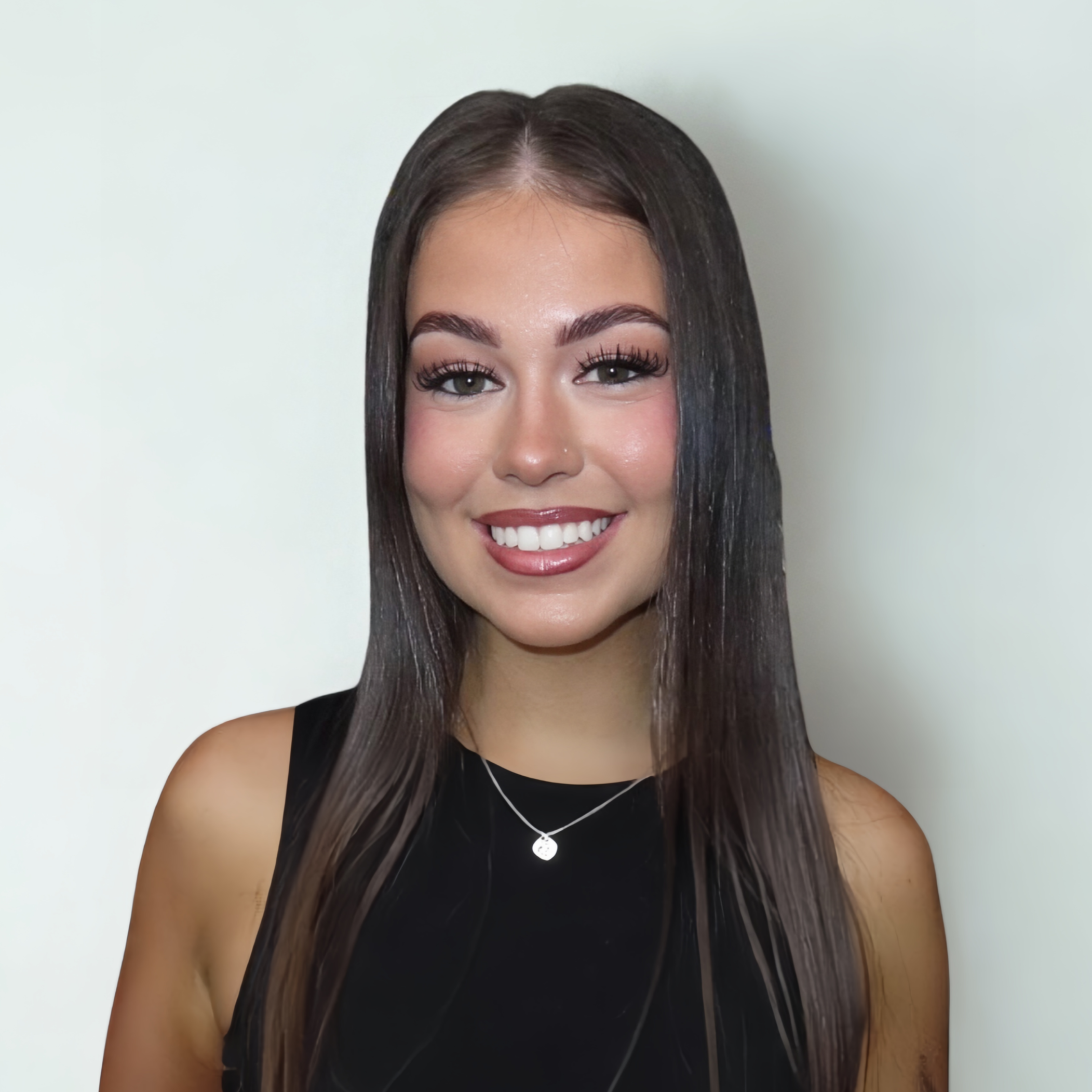 A young woman with long dark hair smiling at the camera, wearing a black sleeveless top and a silver necklace with a small pendant.
