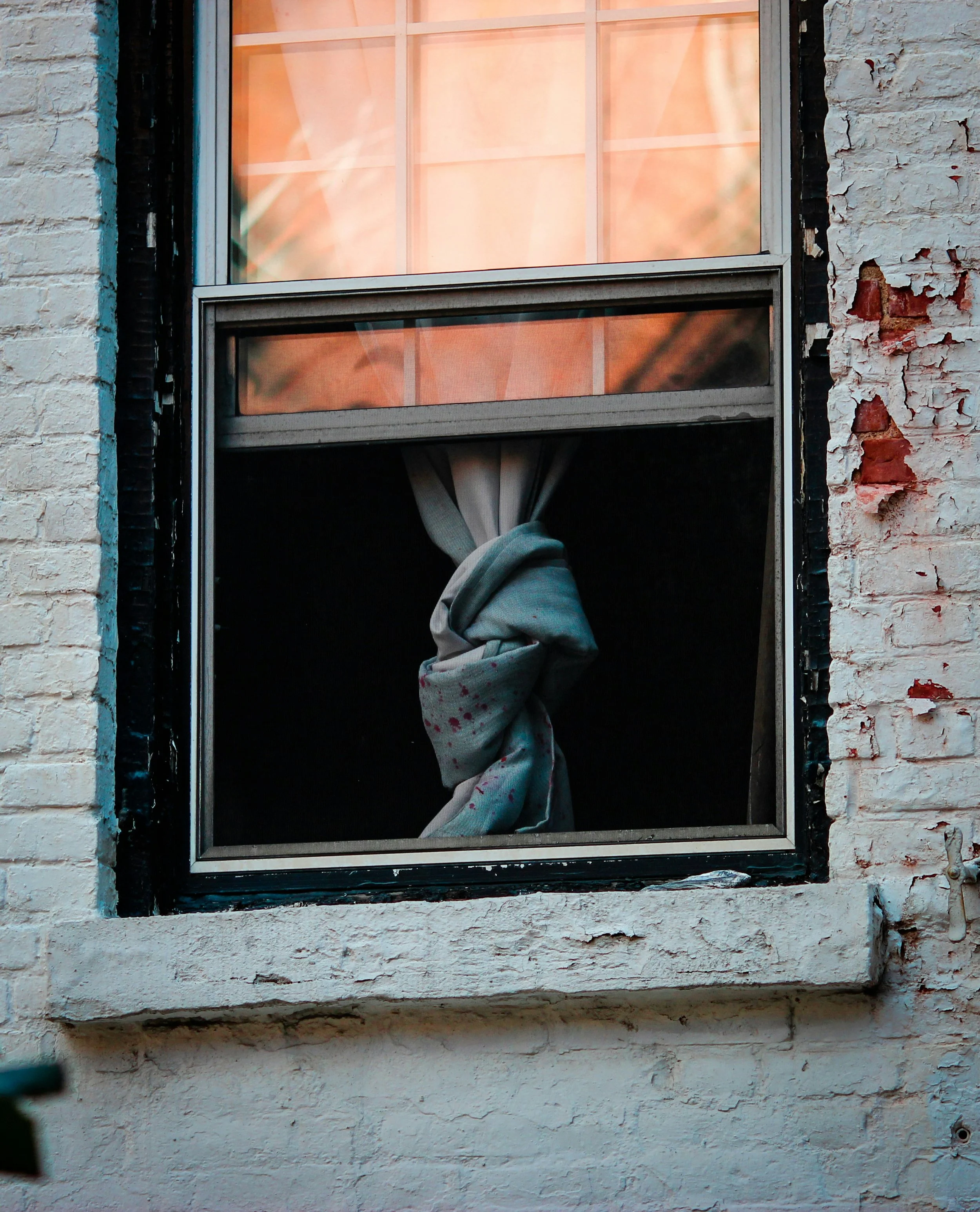 A brick building with a window that is partly open, showing a curtain tied up inside.