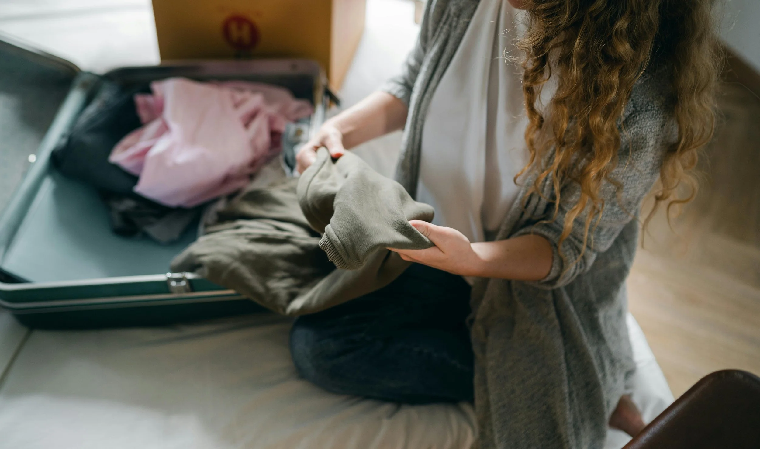 A woman packing a suitcase with clothes, sitting on a bed.