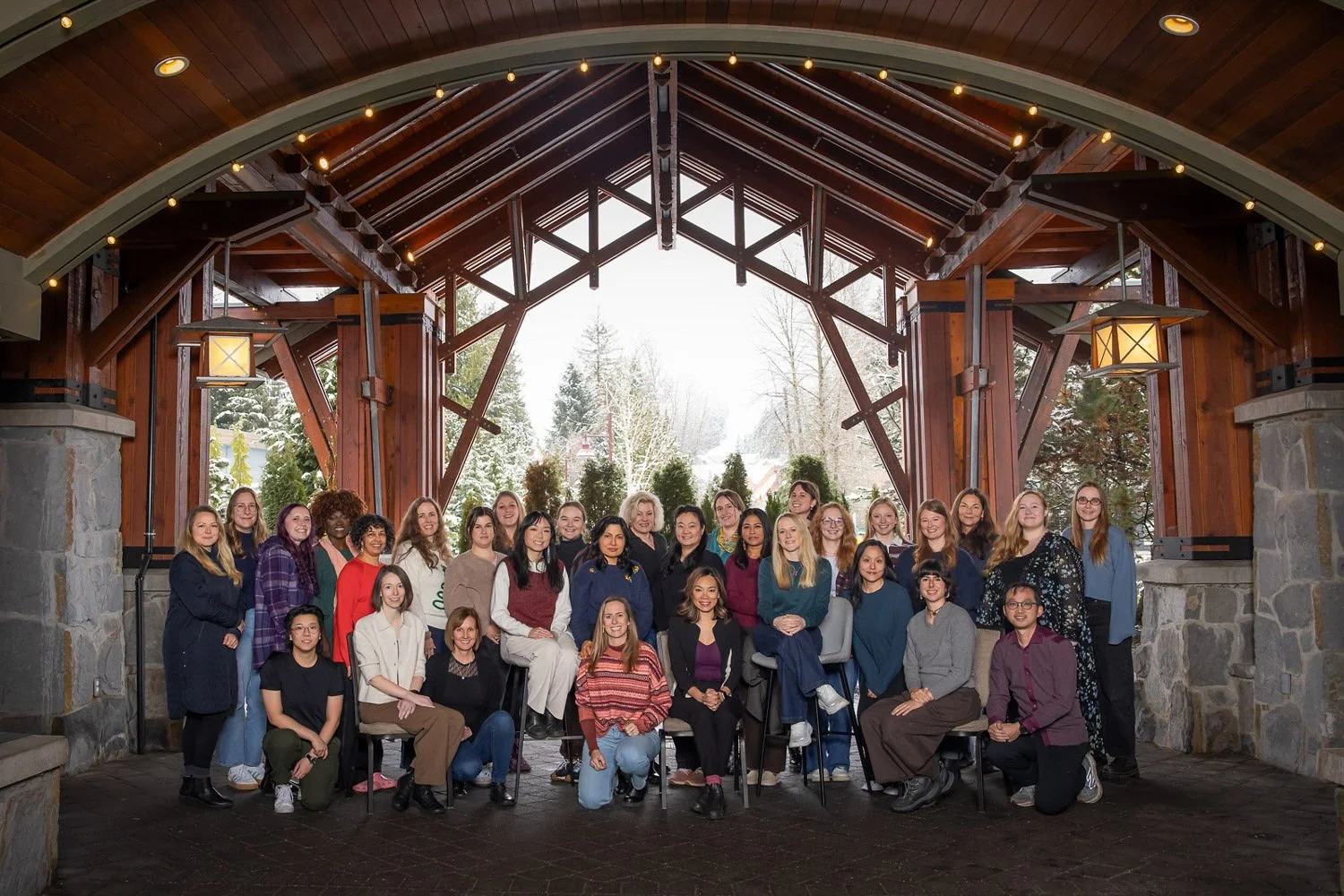 Group photo of diverse women posing indoors with a scenic snowy outdoor background.