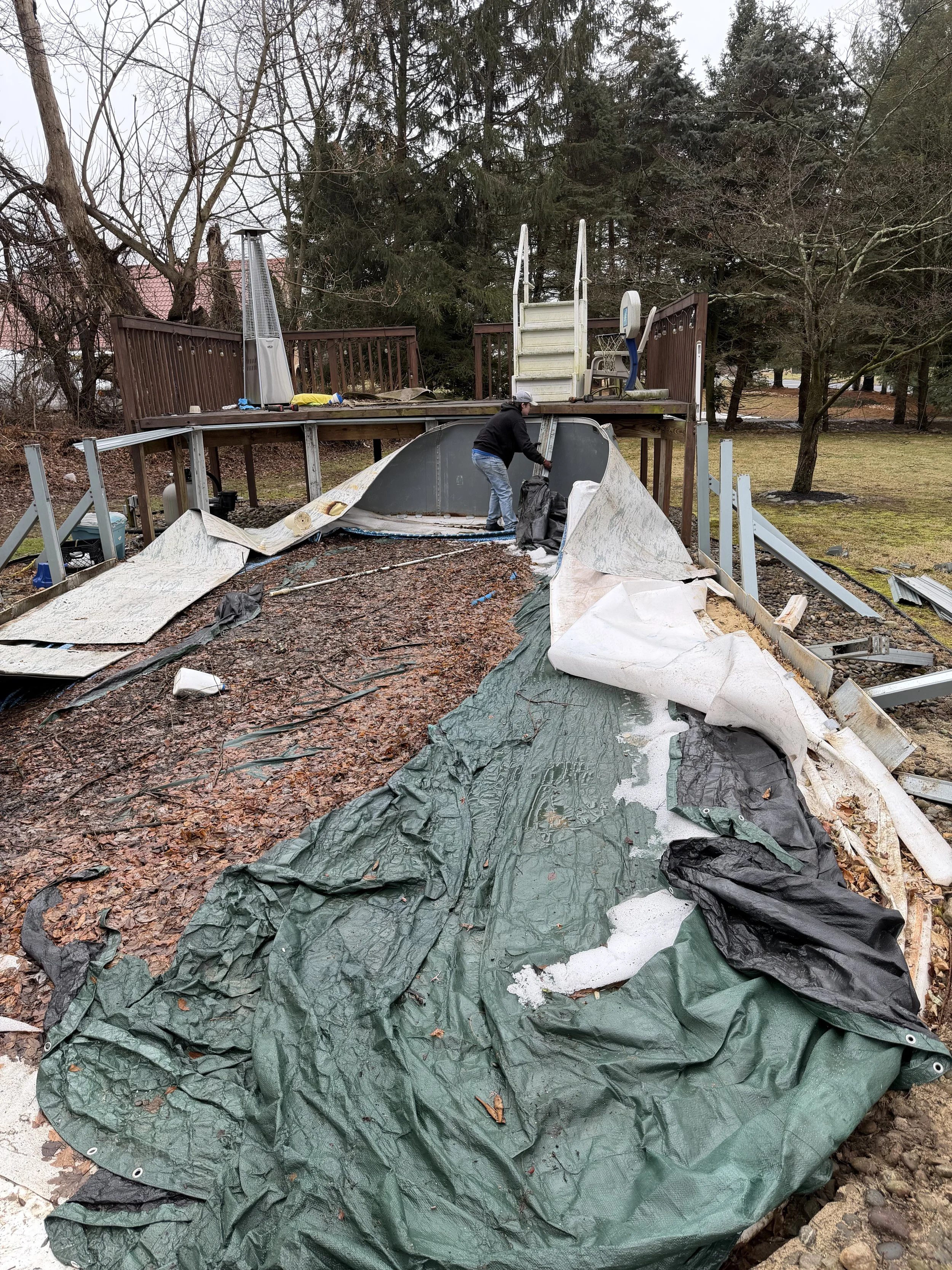 A person is working on removing or repairing a collapsed or damaged inflatable outdoor structure, like a poolside splash pad or bouncy castle, with torn and scattered fabric and debris around.