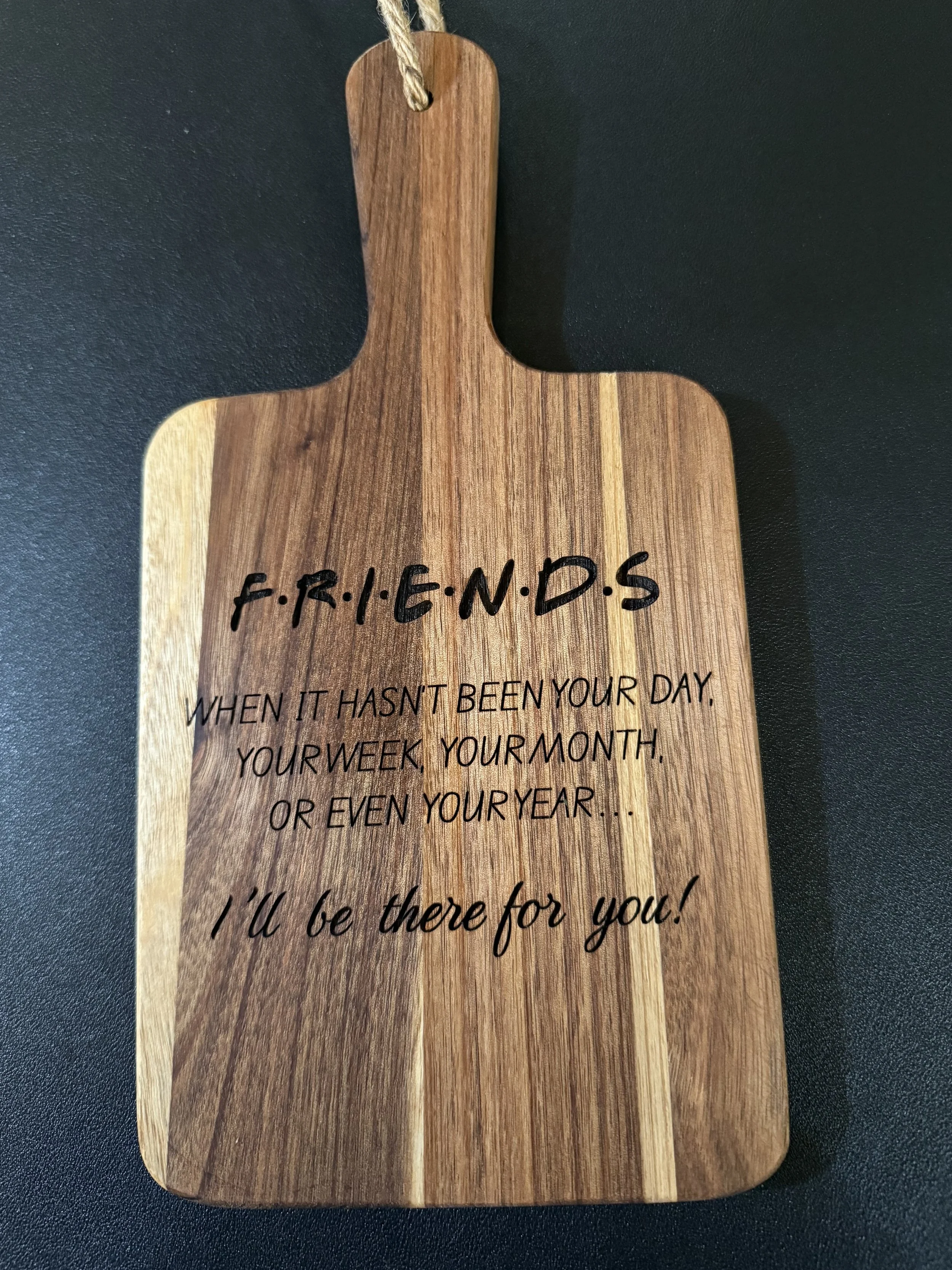 A wooden cutting board shaped like a person with a handle at the top, featuring the word 'FRIENDS' written across the chest area, and an inspirational quote underneath.