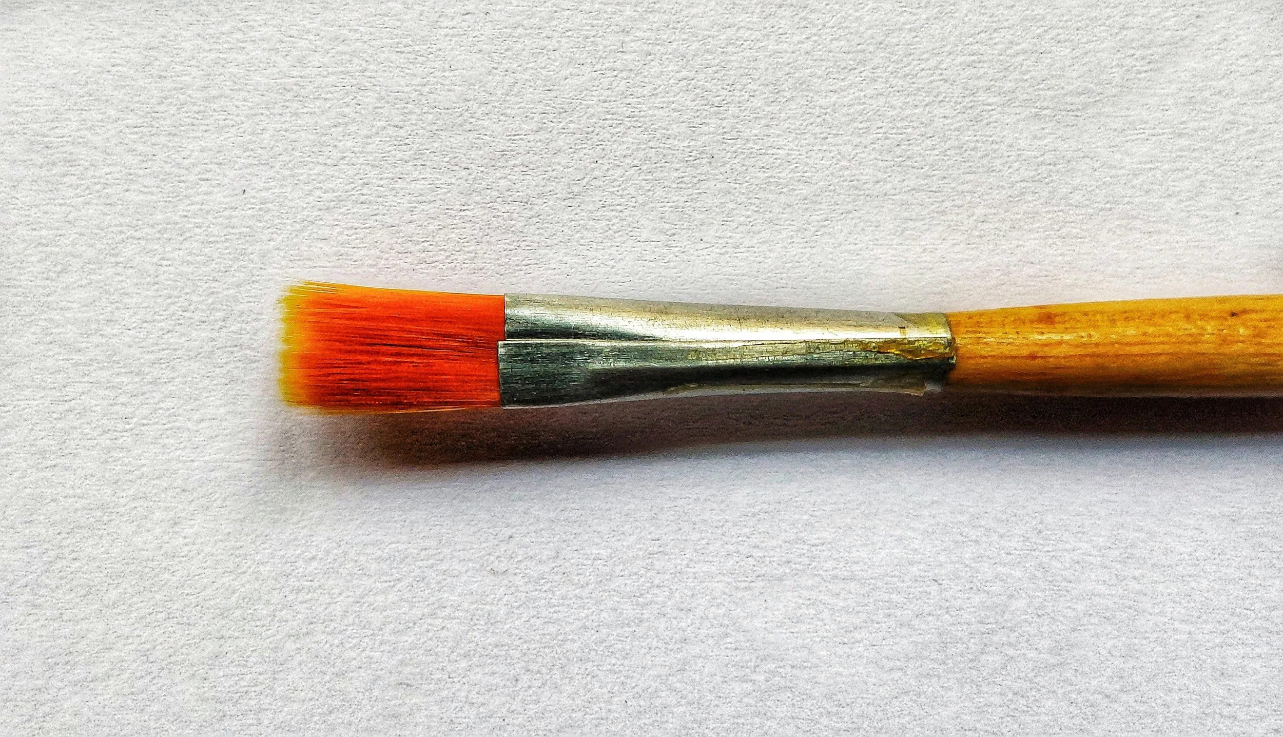Close-up of a paintbrush with red and yellow bristles on a white surface.