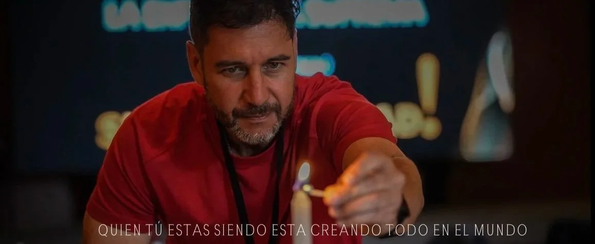 Hombre con barba y camiseta roja, encendiendo una vela con un fósforo en un entorno oscuro.