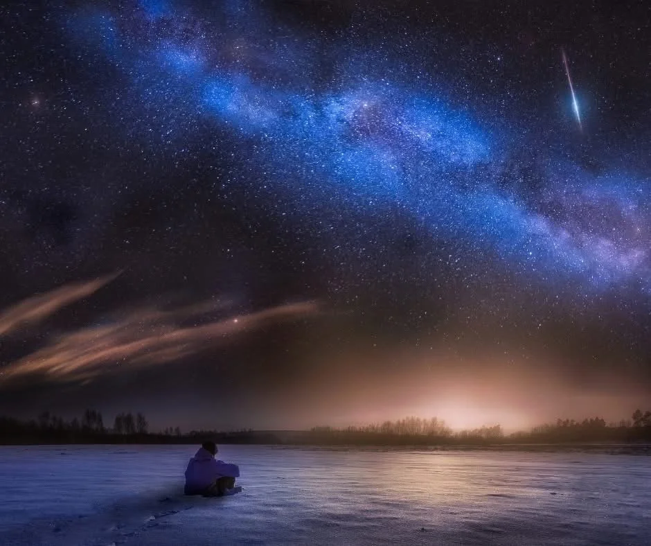 Persona sentada en la orilla de un río viendo el cielo estrellado y la Vía Láctea.