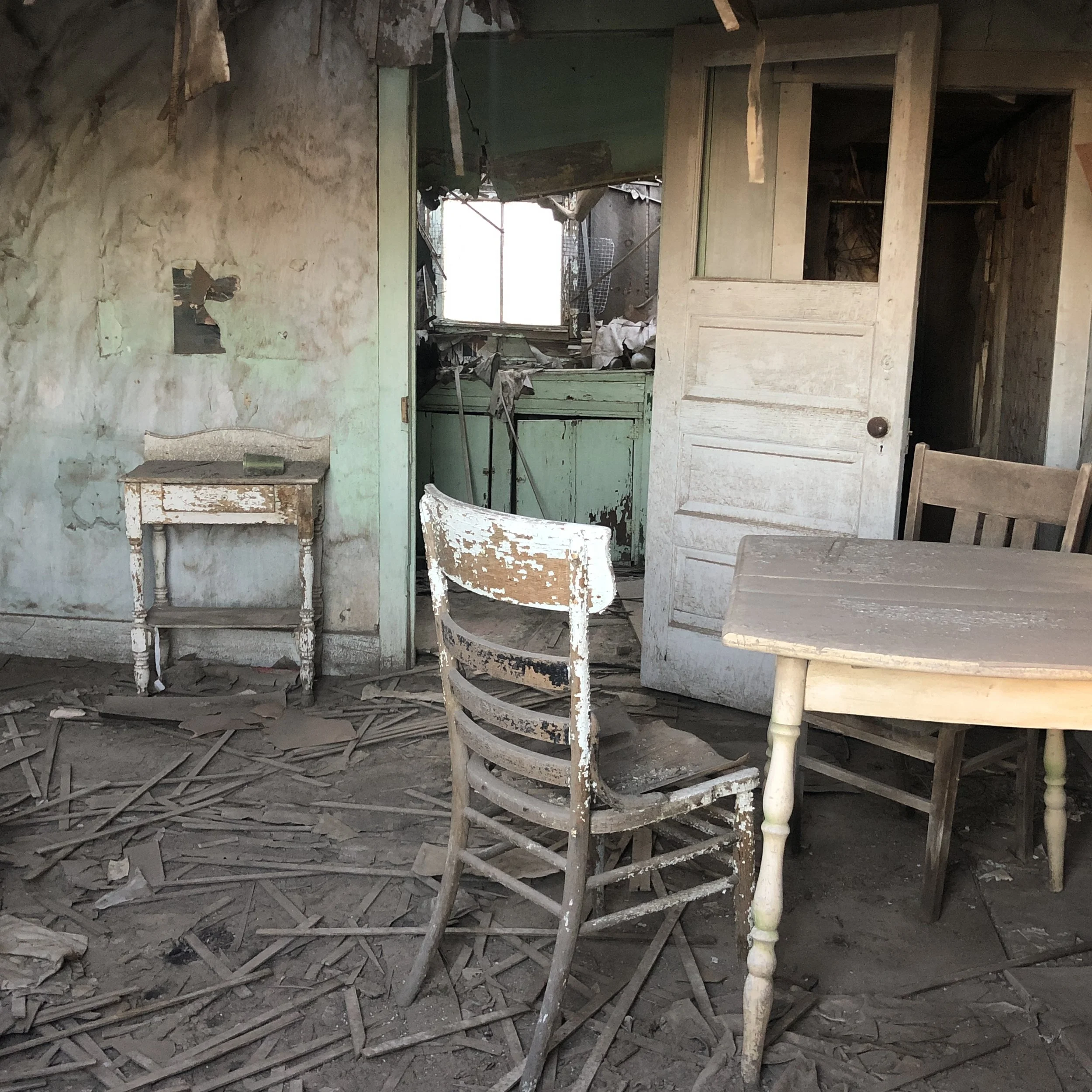 Inside an abandoned, dilapidated house with dusty, broken furniture and dirt-covered floors.