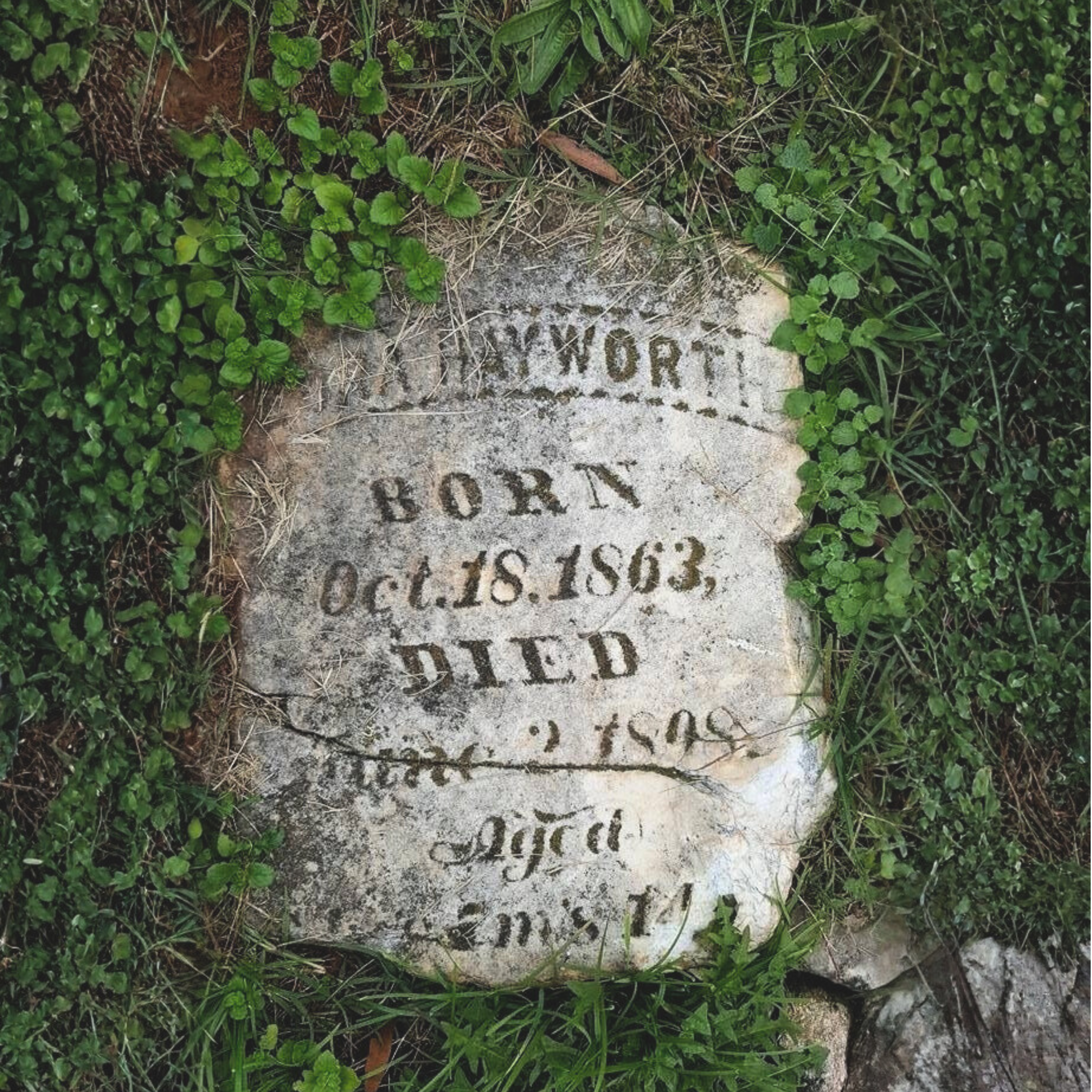 An old headstone partially buried in the grass, dating 1863 - 1898