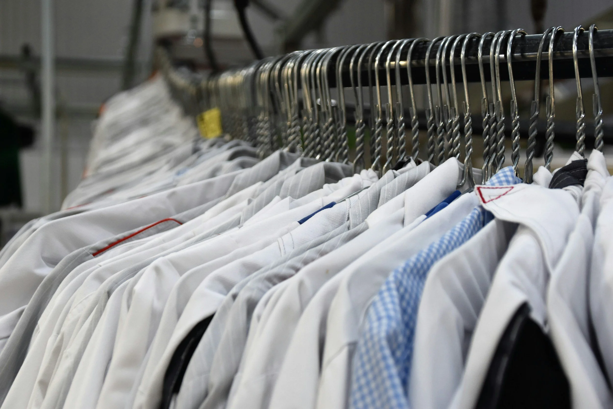 Clothes hung on a metal clothing rack, including white shirts and some with blue and checkered patterns.