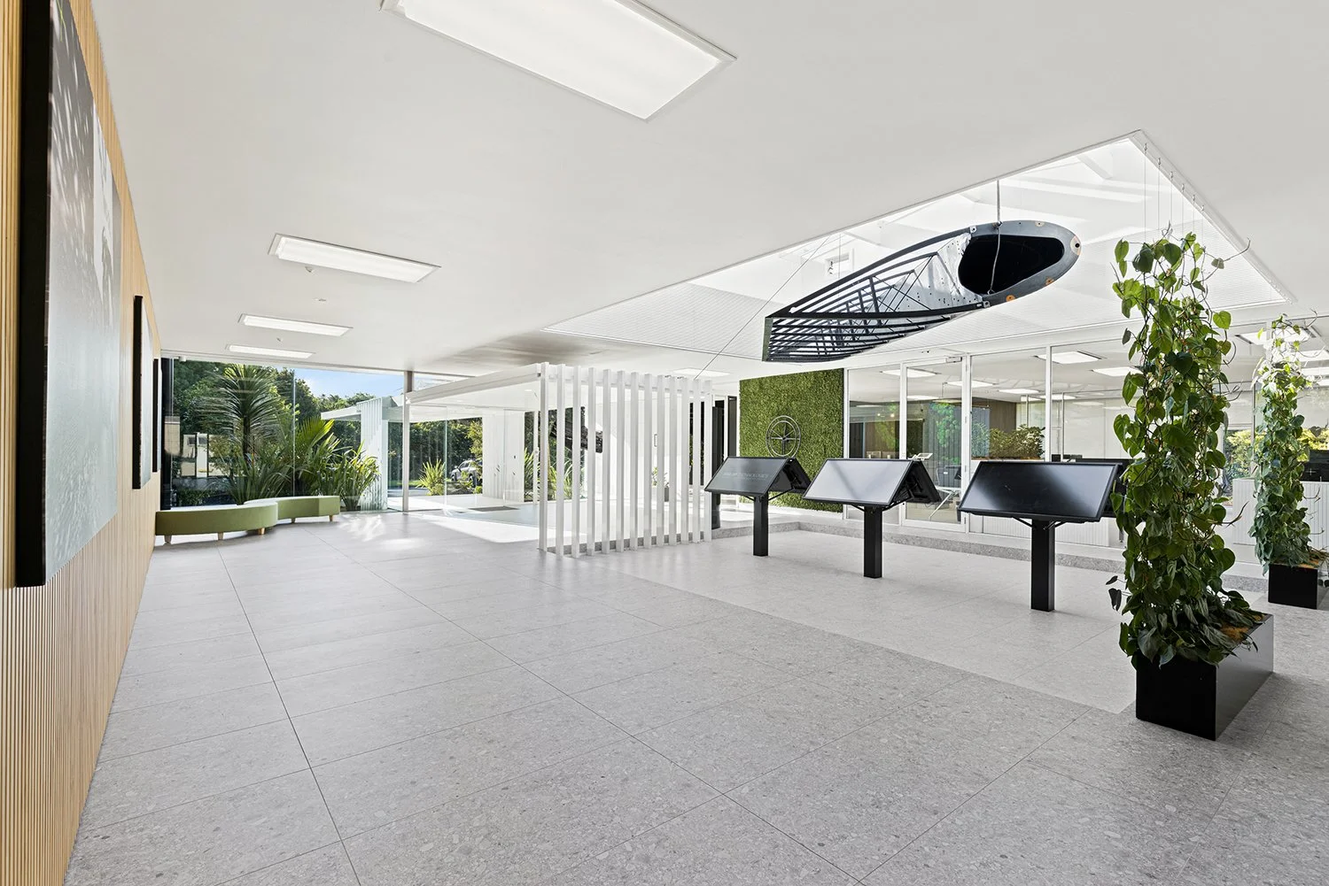 Modern lobby with large windows, green plants, and interactive display screens.