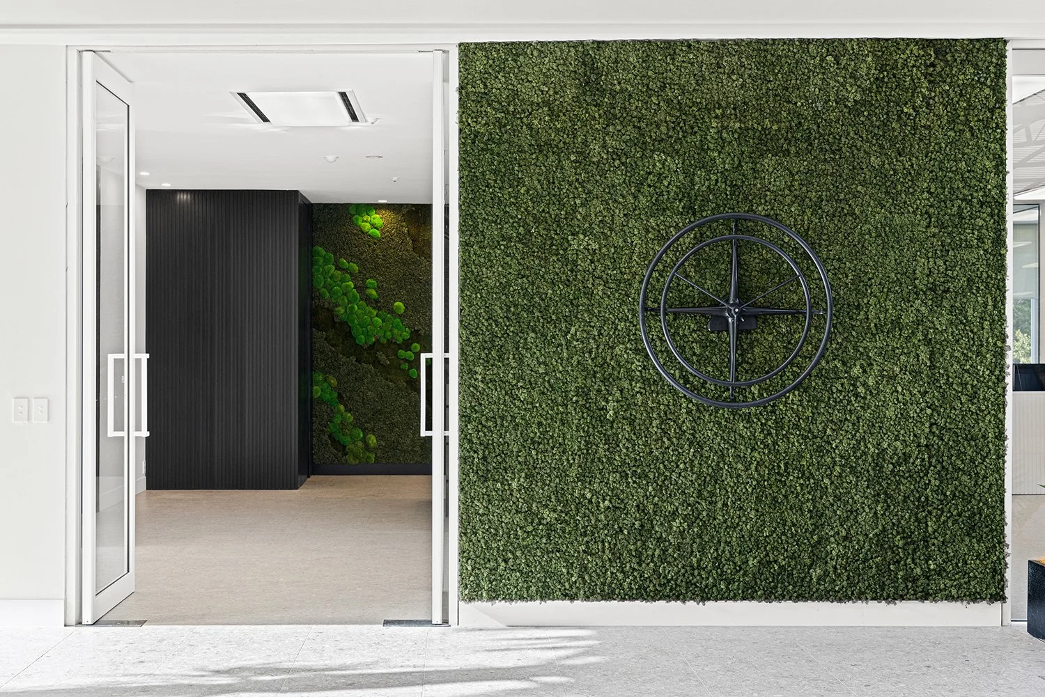 Entryway with glass doors, green wall with moss or plants, and a large black decorative wheel