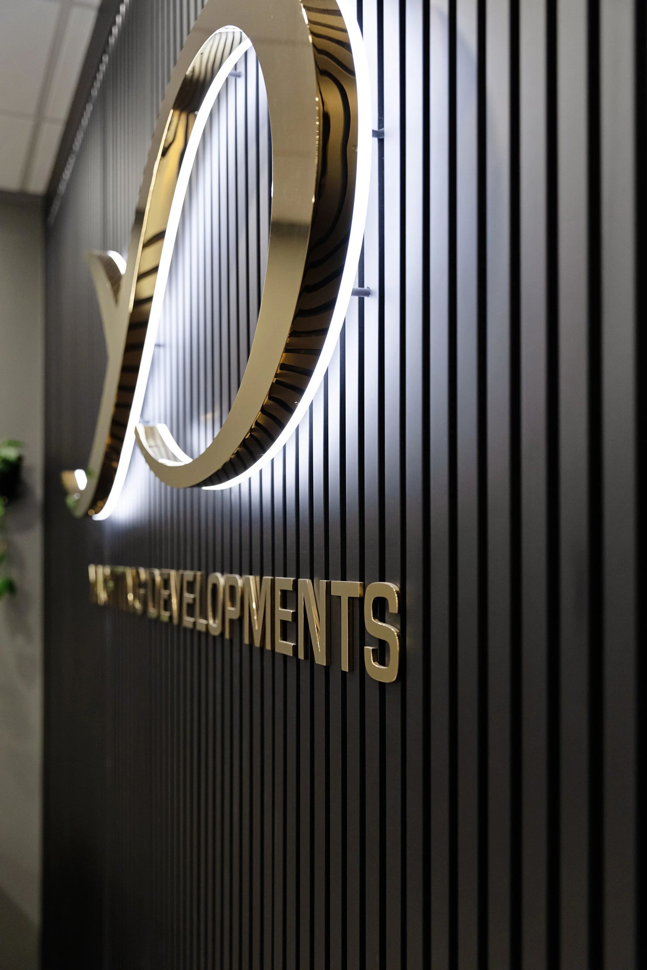 Close-up of a black wall with a metallic sign that says 'DEVELOPMENTS' mounted on it, with the letter 'O' designed as a stylized circular logo surrounding the word.