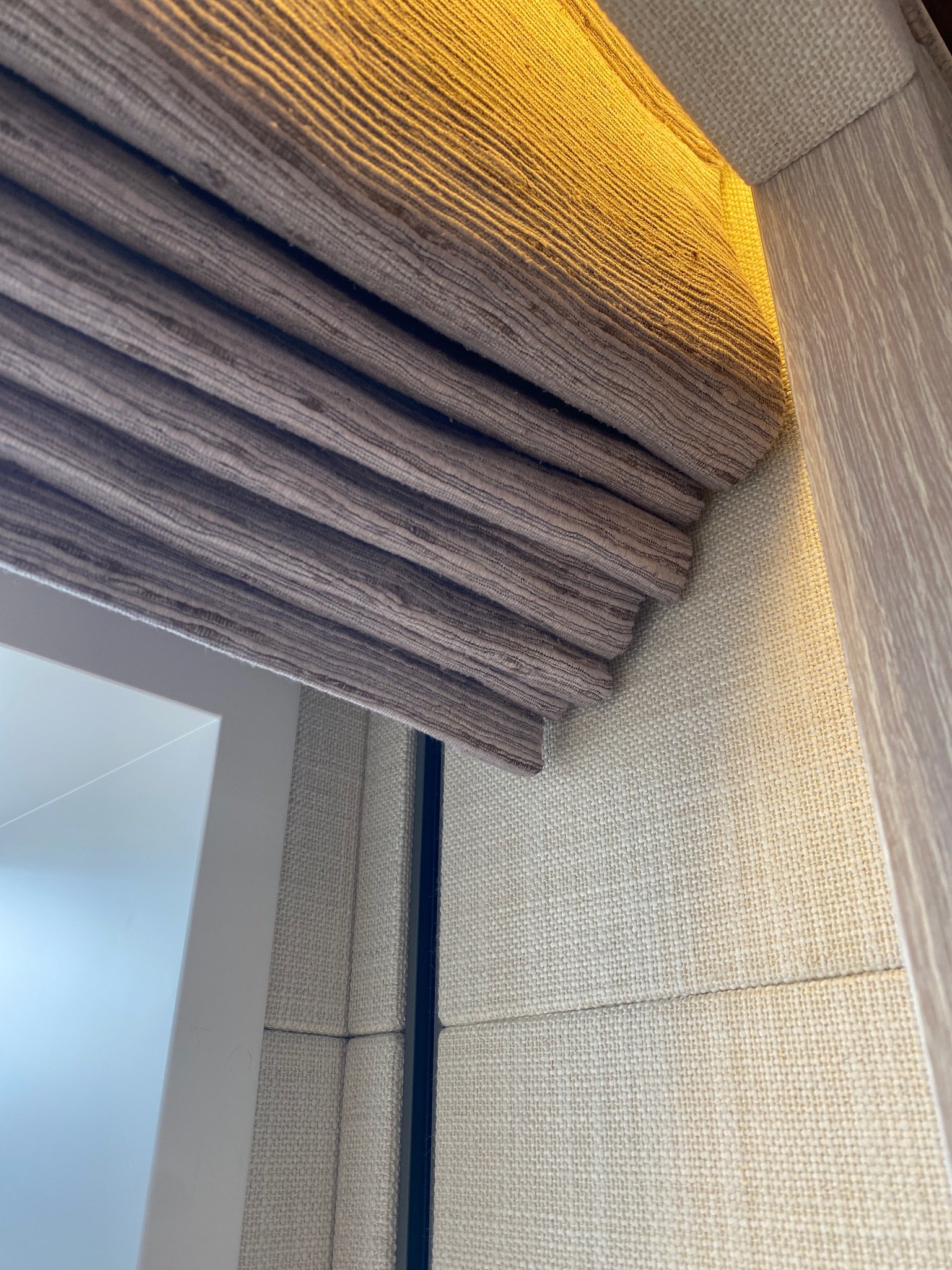 Close-up of a sofa with multiple cushions, covered with a textured beige and brown striped fabric. The photo is taken at an angle, showing the corner of the sofa with a small wooden table beside it.