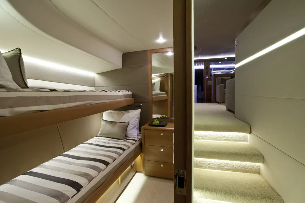Interior of a small, modern sleeping area with bunk beds, pillows, a mirror, and a staircase leading to a living room area with seating.
