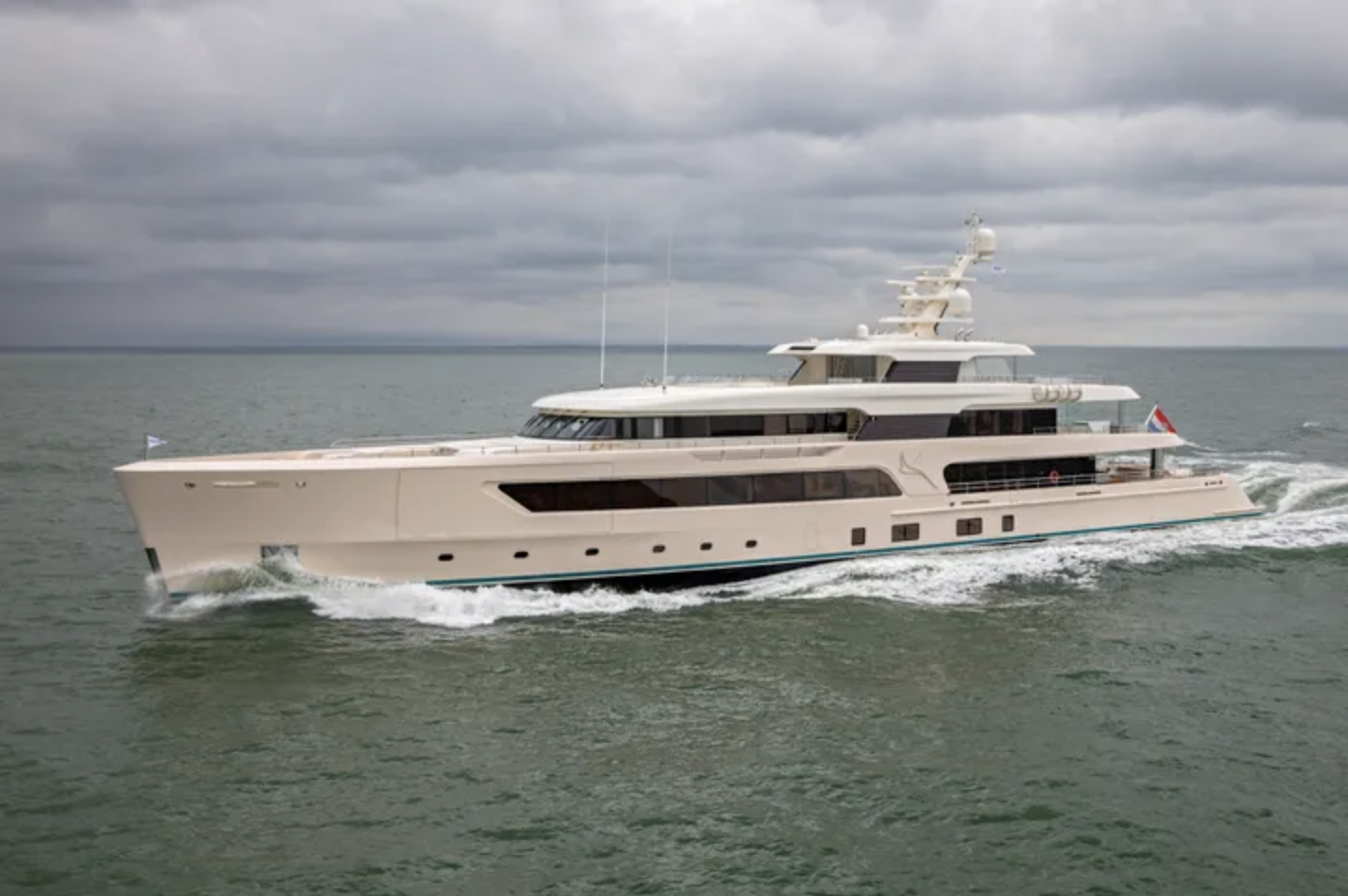 Large white luxury yacht sailing on calm water under a cloudy sky.