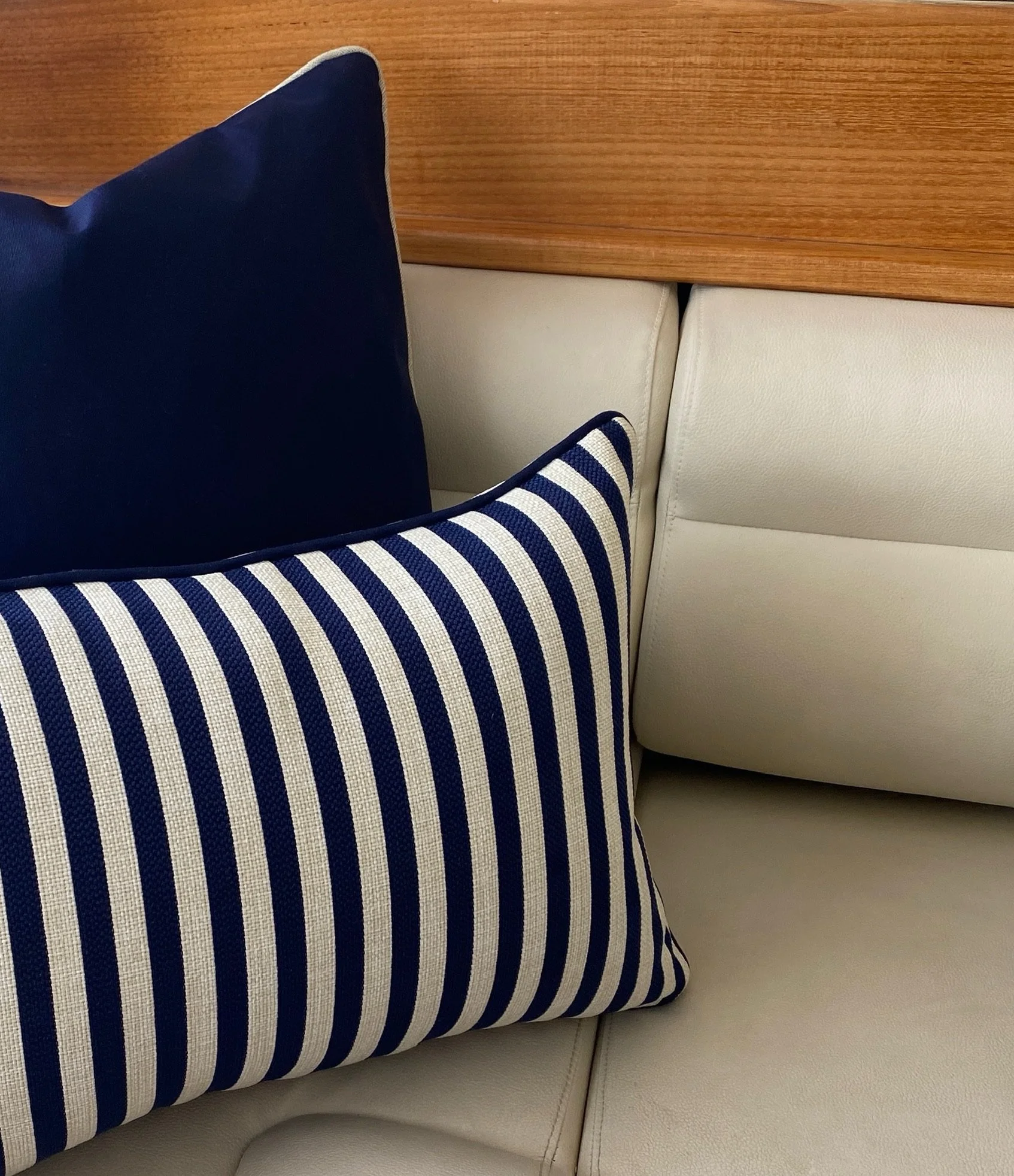 Close-up of a striped blue and white pillow on a cream-colored sofa, with a plain wooden headboard in the background.