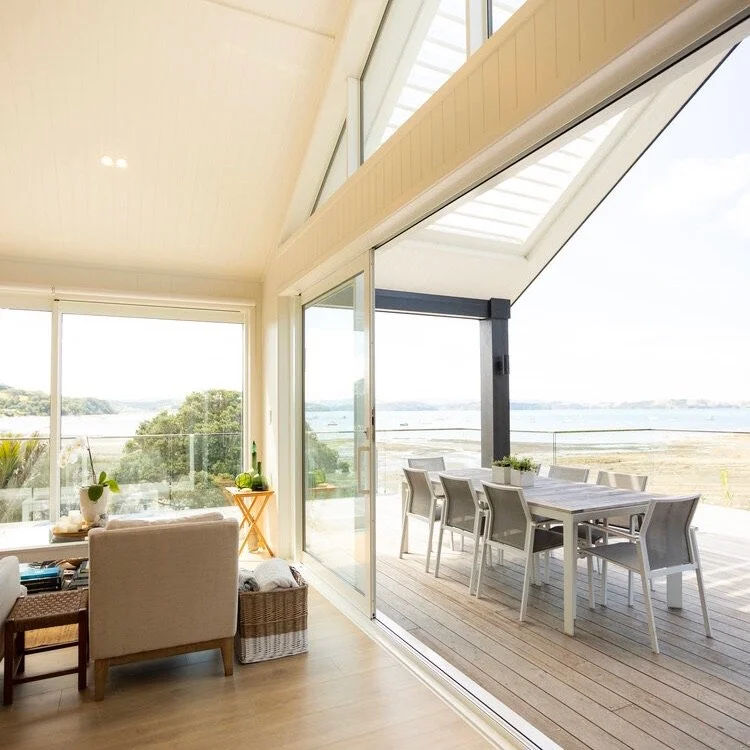 A bright living room with large sliding glass doors leading to an outdoor deck overlooking a body of water and a landscape with trees and open land.