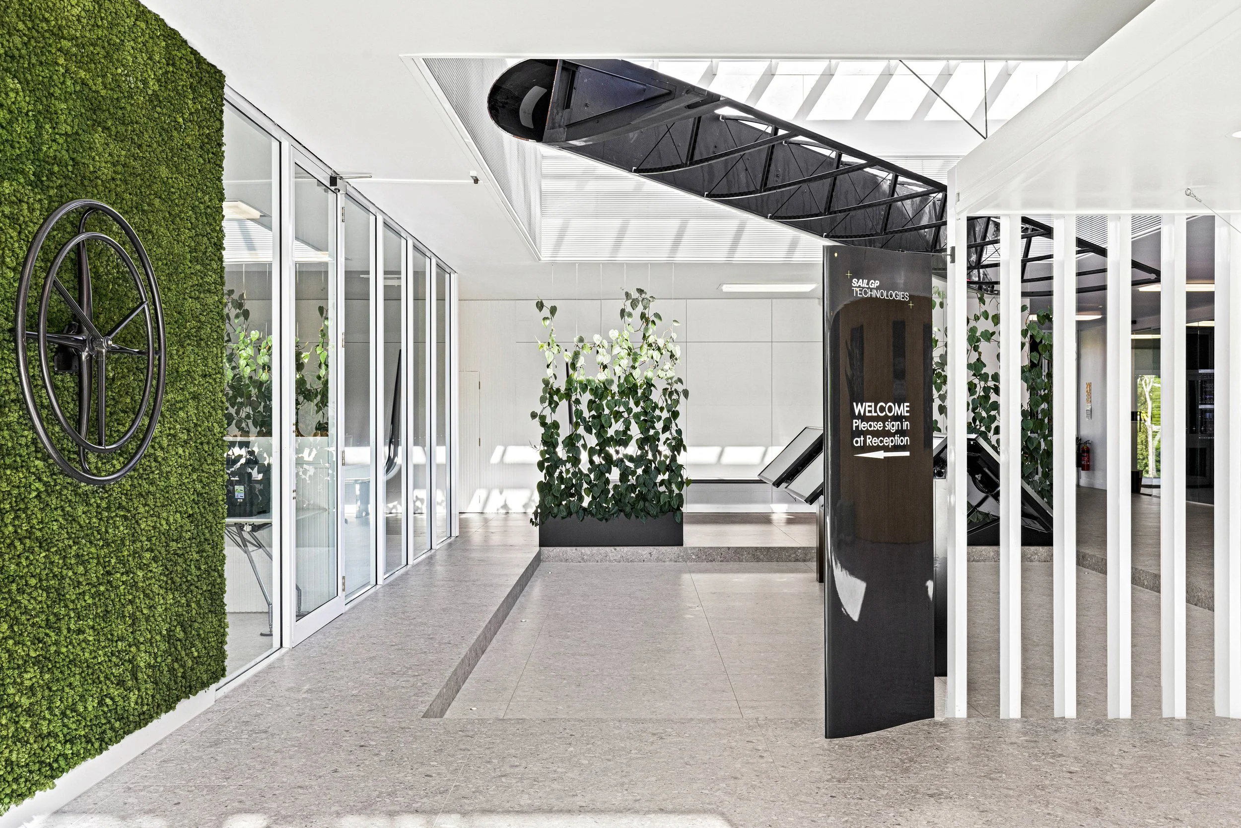 Modern office reception area with green wall, glass doors, plants, and a black sculpture of a ship's bow.