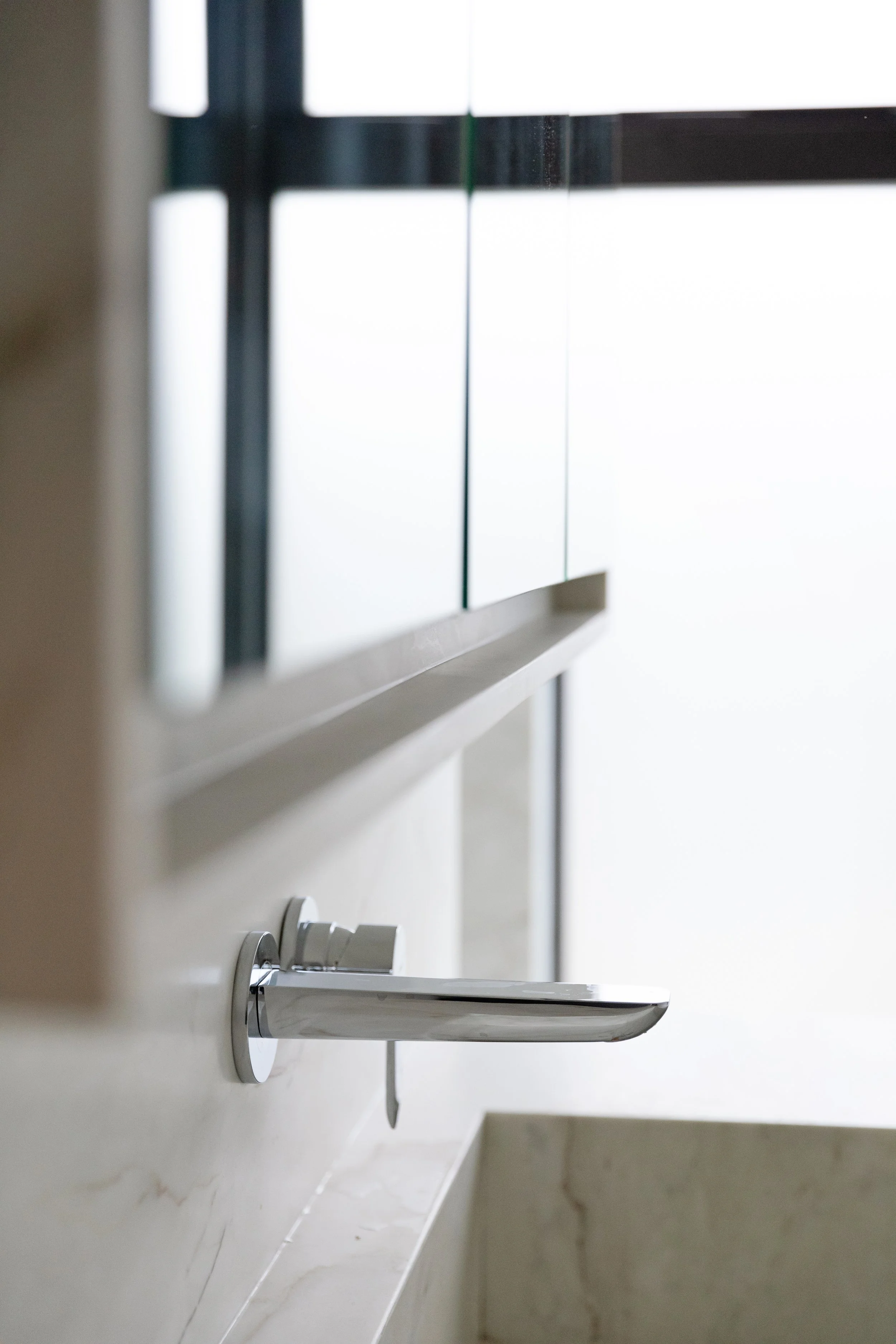 Close-up of a modern silver kitchen faucet mounted on a light-colored marble countertop in a well-lit kitchen area.