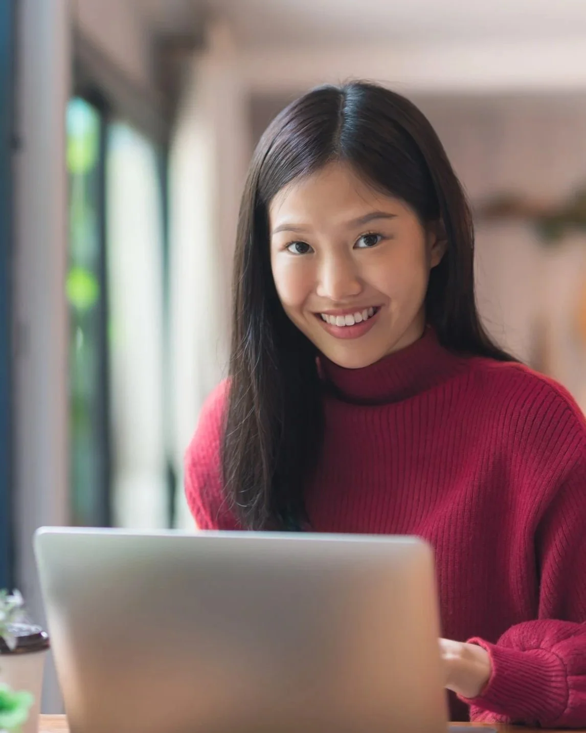 Foster child with long dark hair and a red sweater smiling at a laptop.
