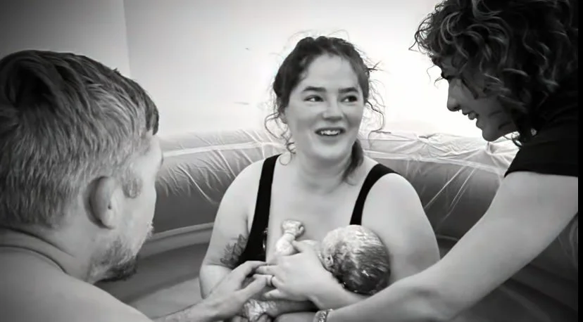 Midwife smiling at a couple who just caught their baby in a birth tub