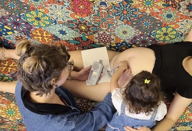 Mother giving birth with her partner and young child present, in a colorful room.