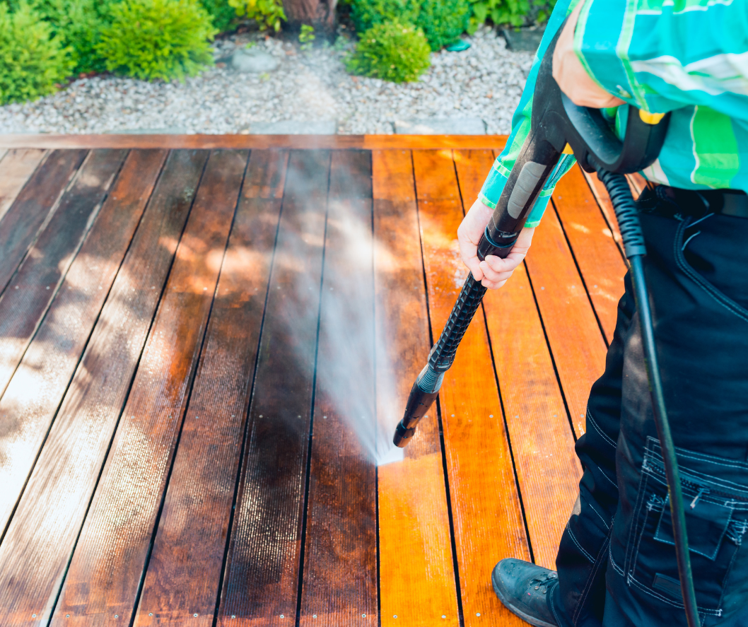 Child using a pressure washer to clean a wooden deck outdoors.