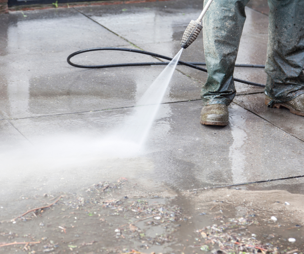 Person pressure washing a wet concrete sidewalk.
