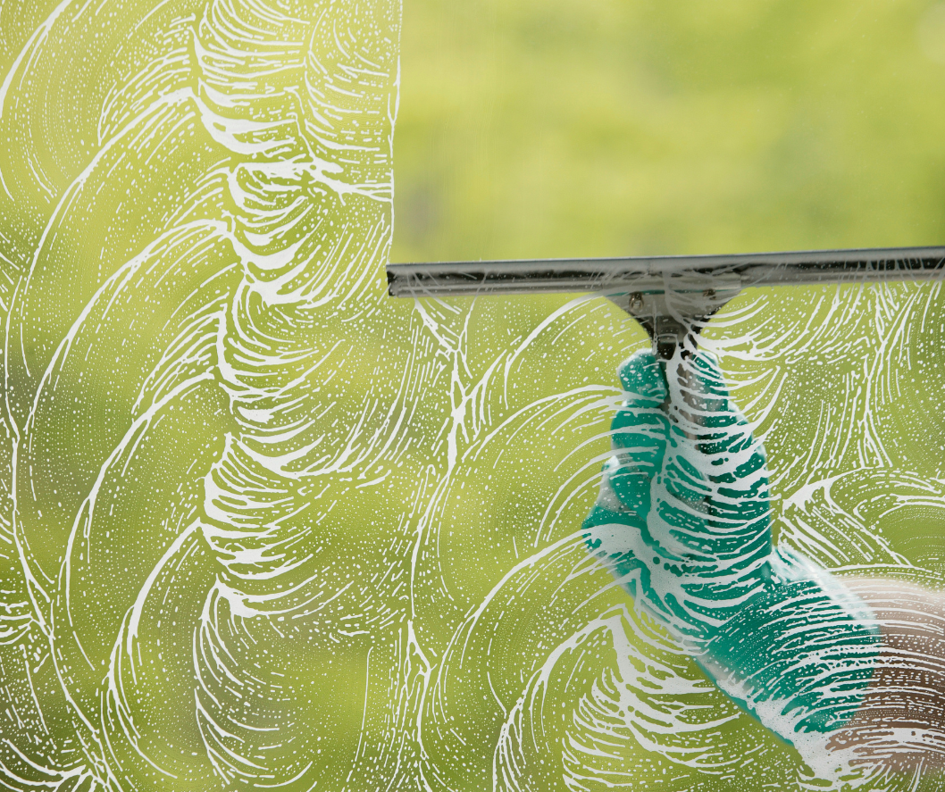 Close-up of a window cleaning process with a squeegee, with soap foam and water on the glass.