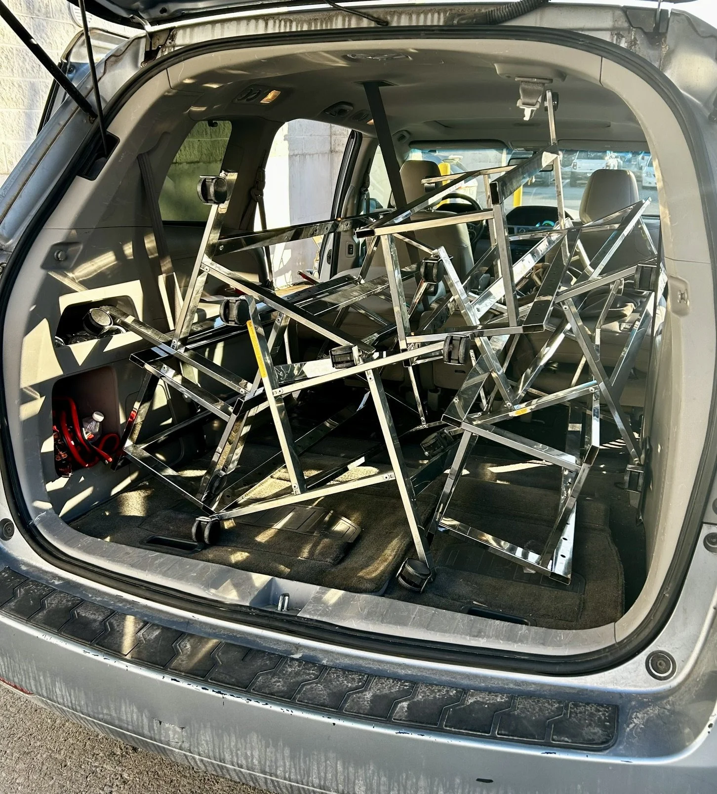 The back of an SUV with the rear door open, filled with metal framing scaffolding or structural supports.